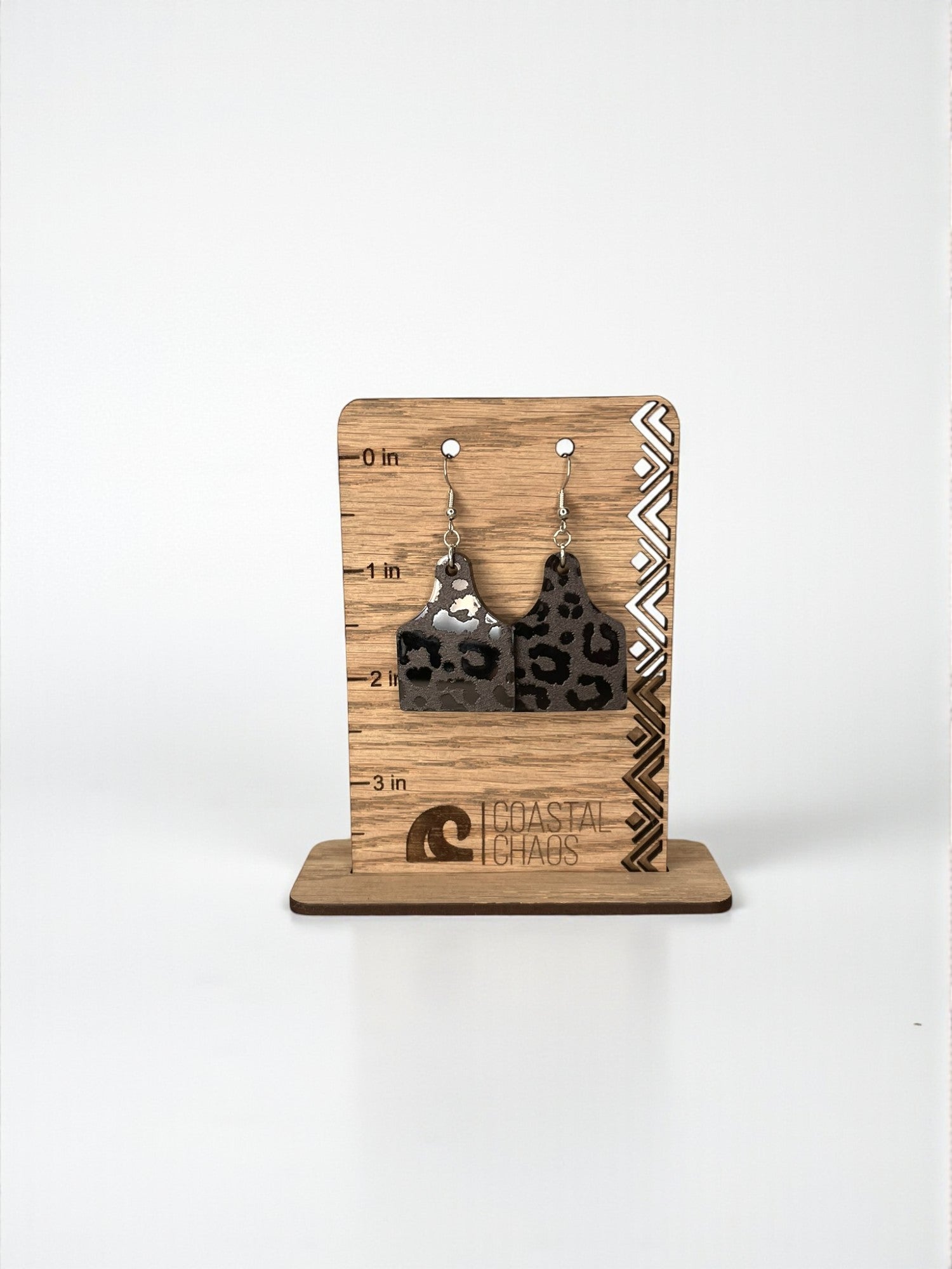 A pair of leopard print earrings displayed on a wooden stand with measurements and a logo.