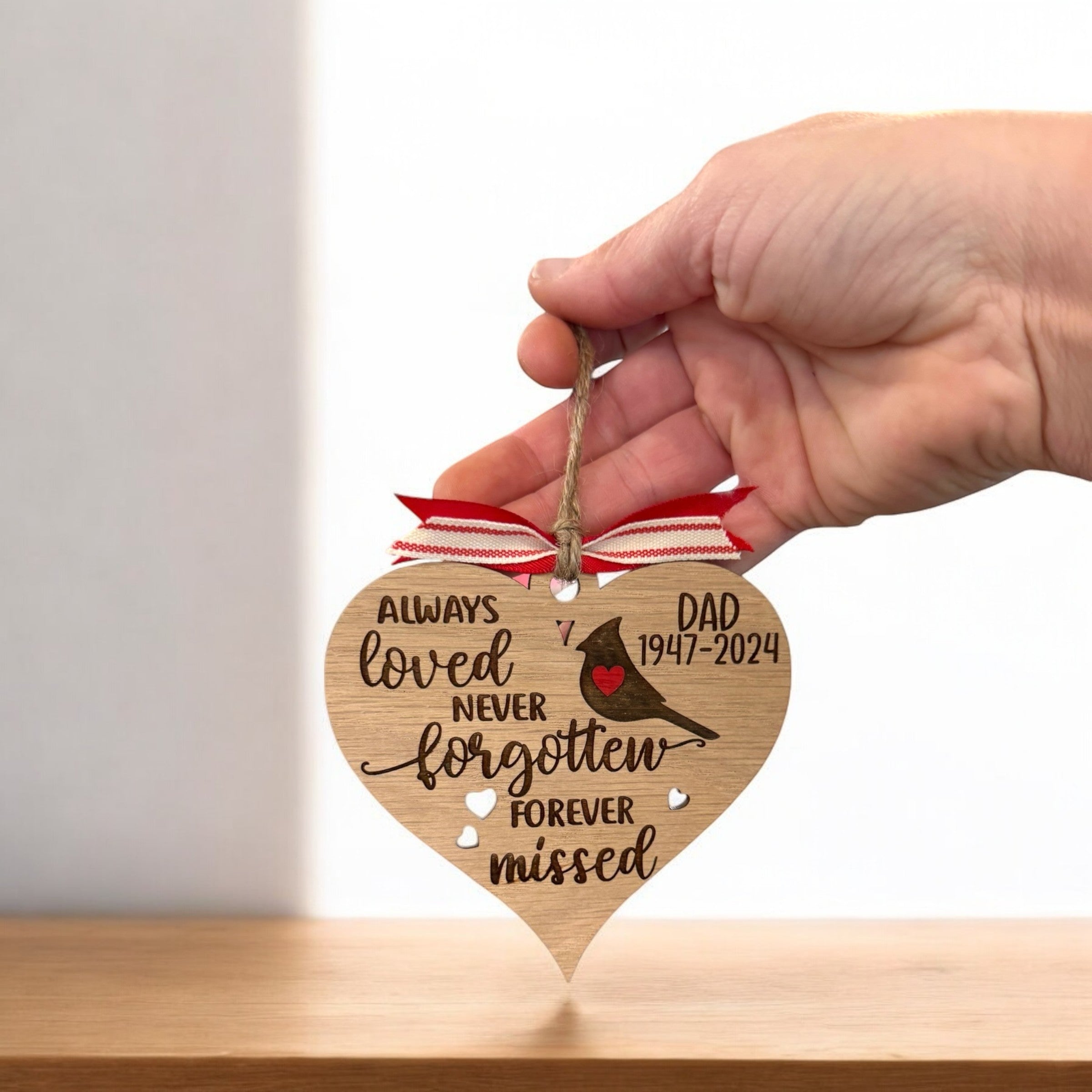 A hand holding a wooden heart-shaped ornament with a ribbon and a message about a father.