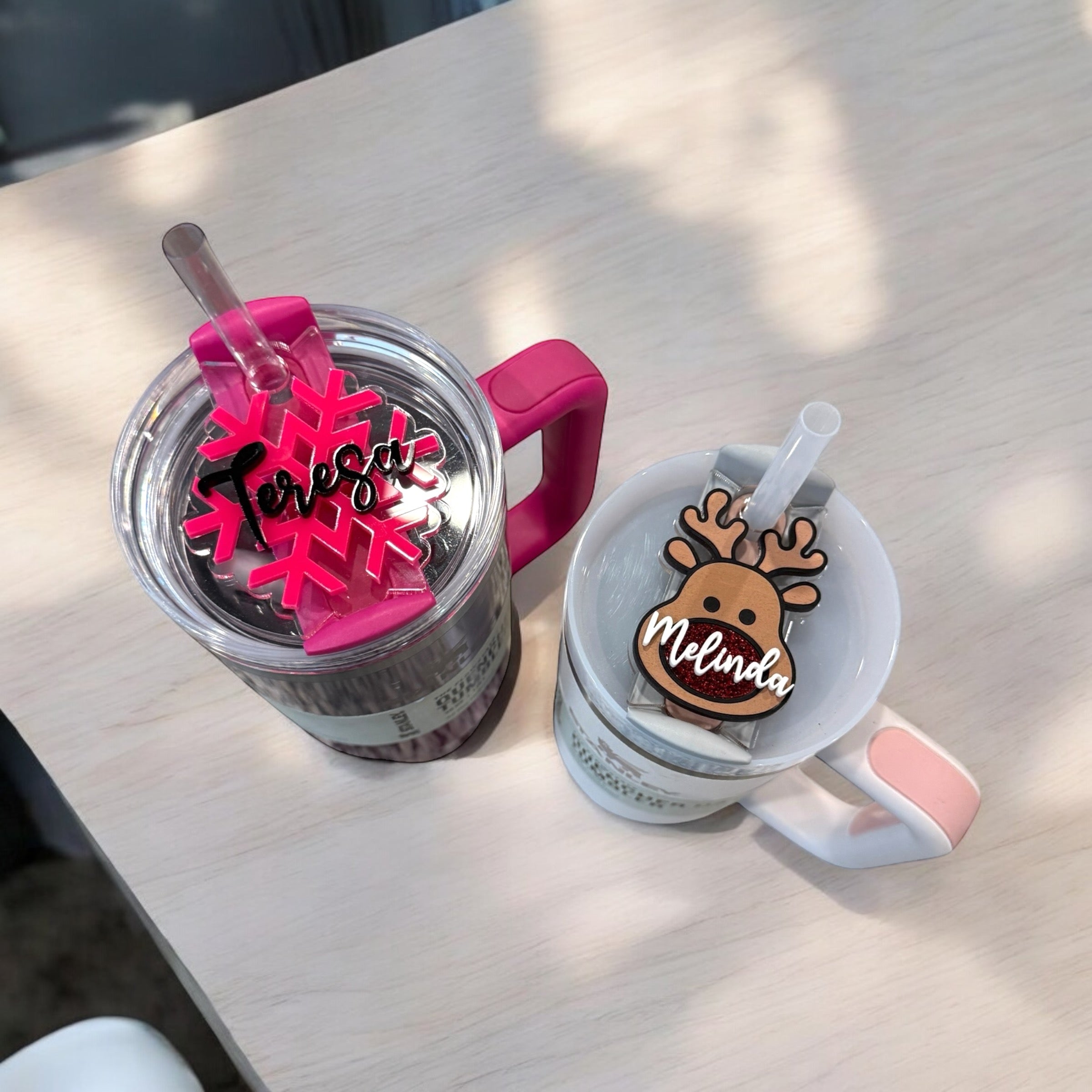 Two mugs with personalized names on them, one with a pink handle and the other with a white handle, sitting on a wooden surface.