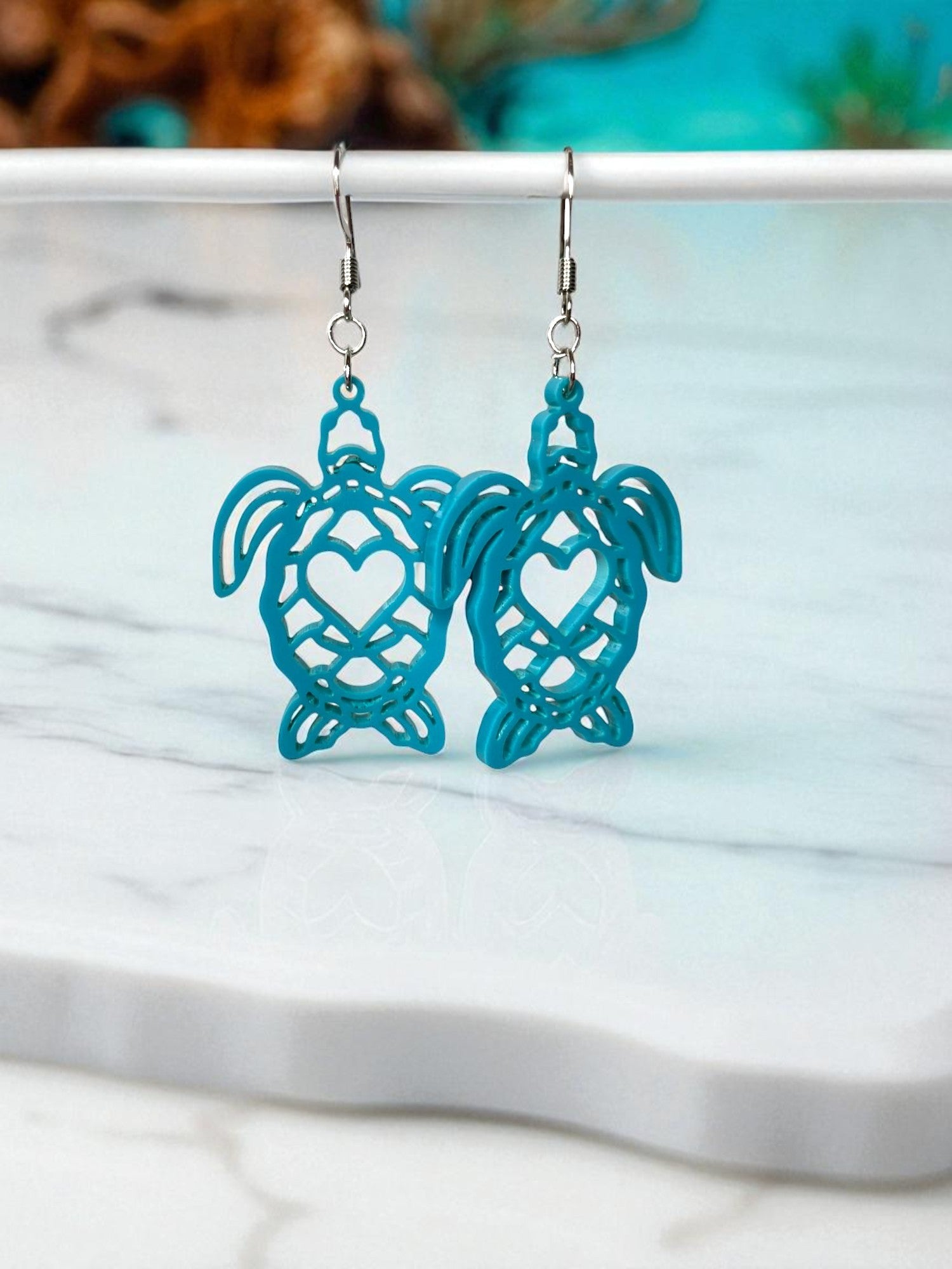 A pair of turquoise earrings with heart-shaped designs, hanging from a white surface.