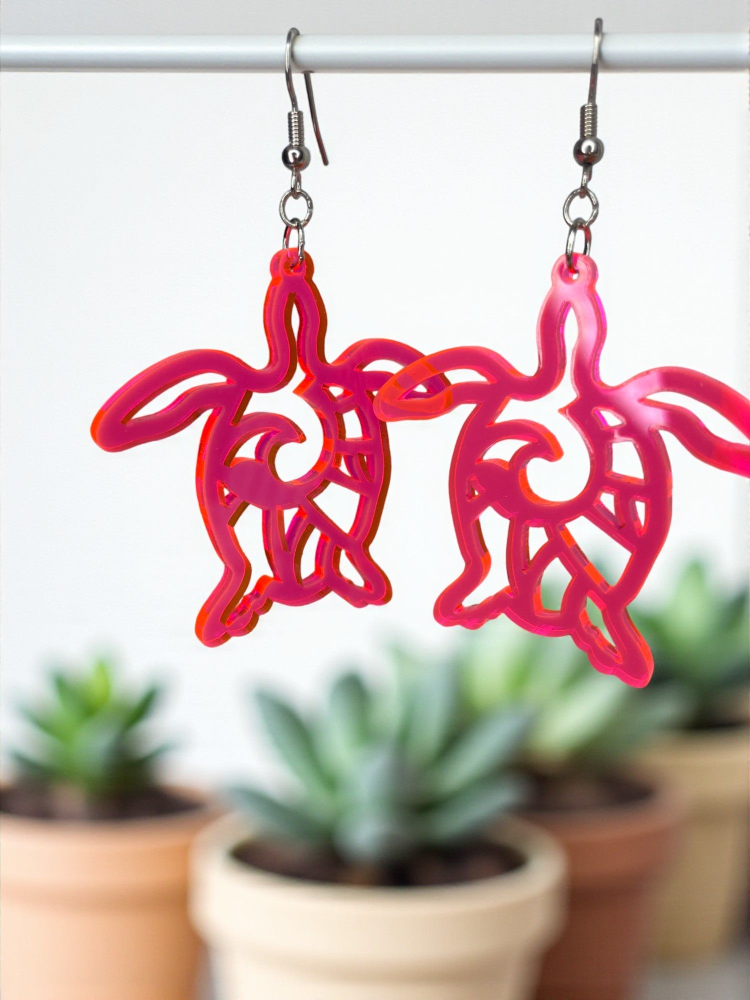A pair of pink earrings with a stylized turtle design hanging from a hook.