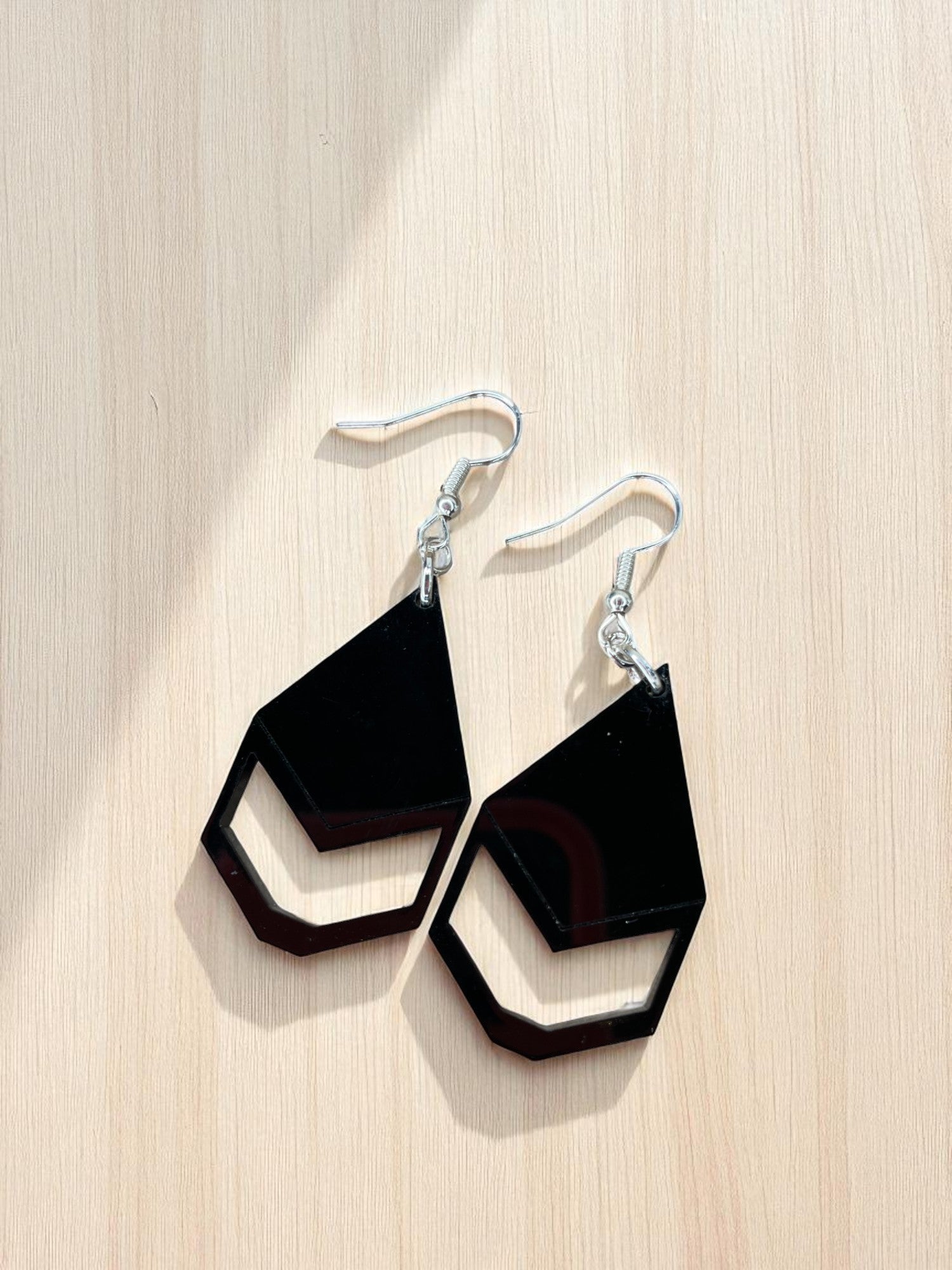 A pair of black geometric earrings with a silver hook and loop design, resting on a wooden surface.