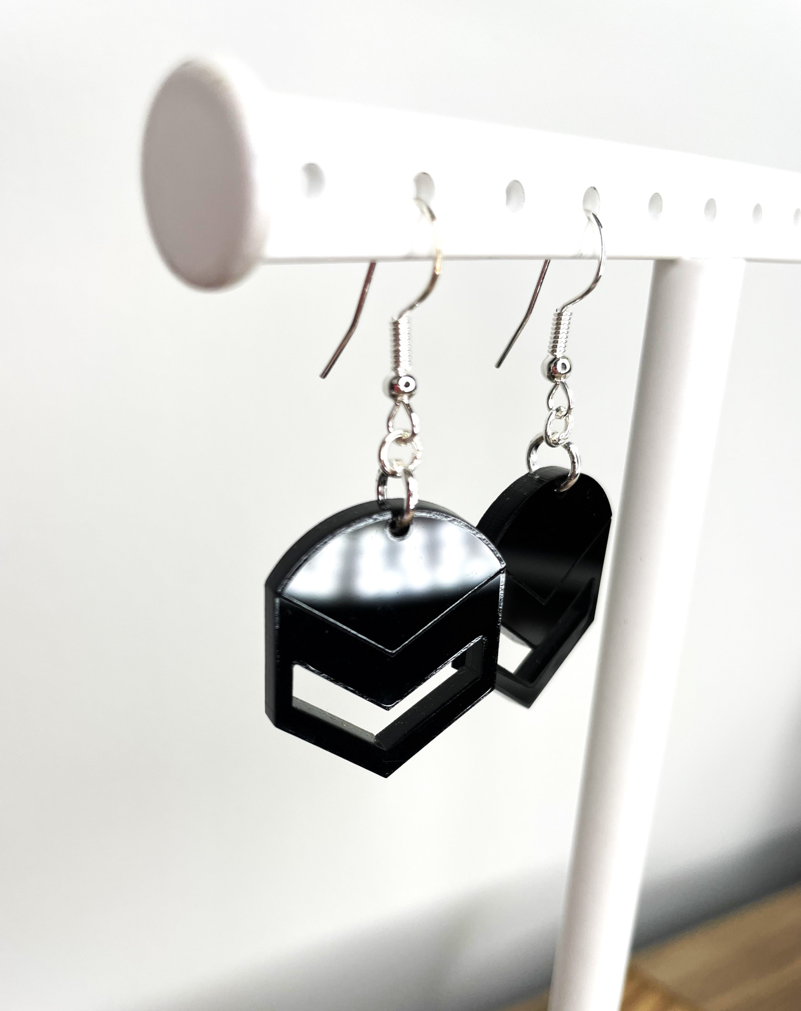 A pair of black earrings with a hexagonal shape hanging from a white metal stand.
