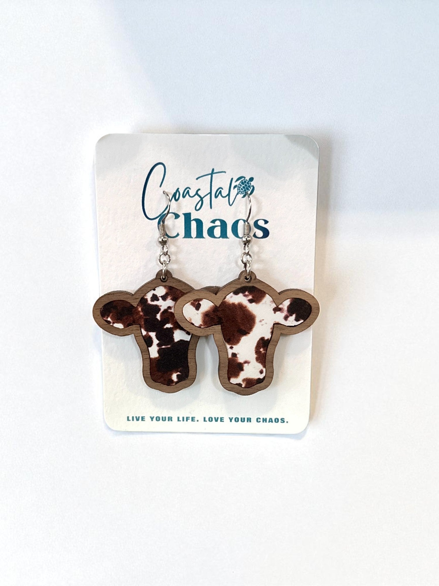 A pair of wooden earrings with a spotted pattern, displayed on a white card with the text "Coastal Chaos" and a motivational quote.