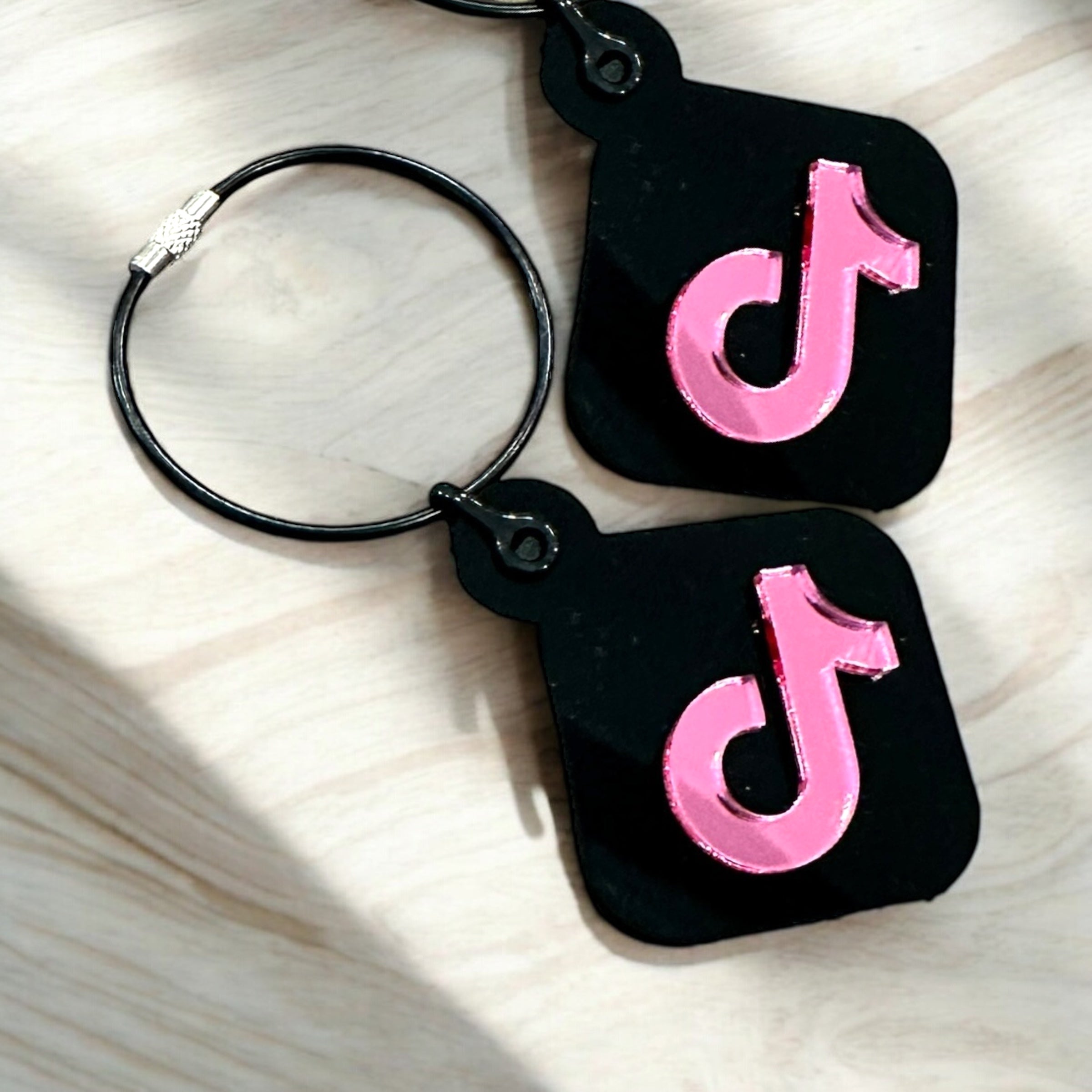 a pair of black keychains with pink and silver versions of the Twitter logo.