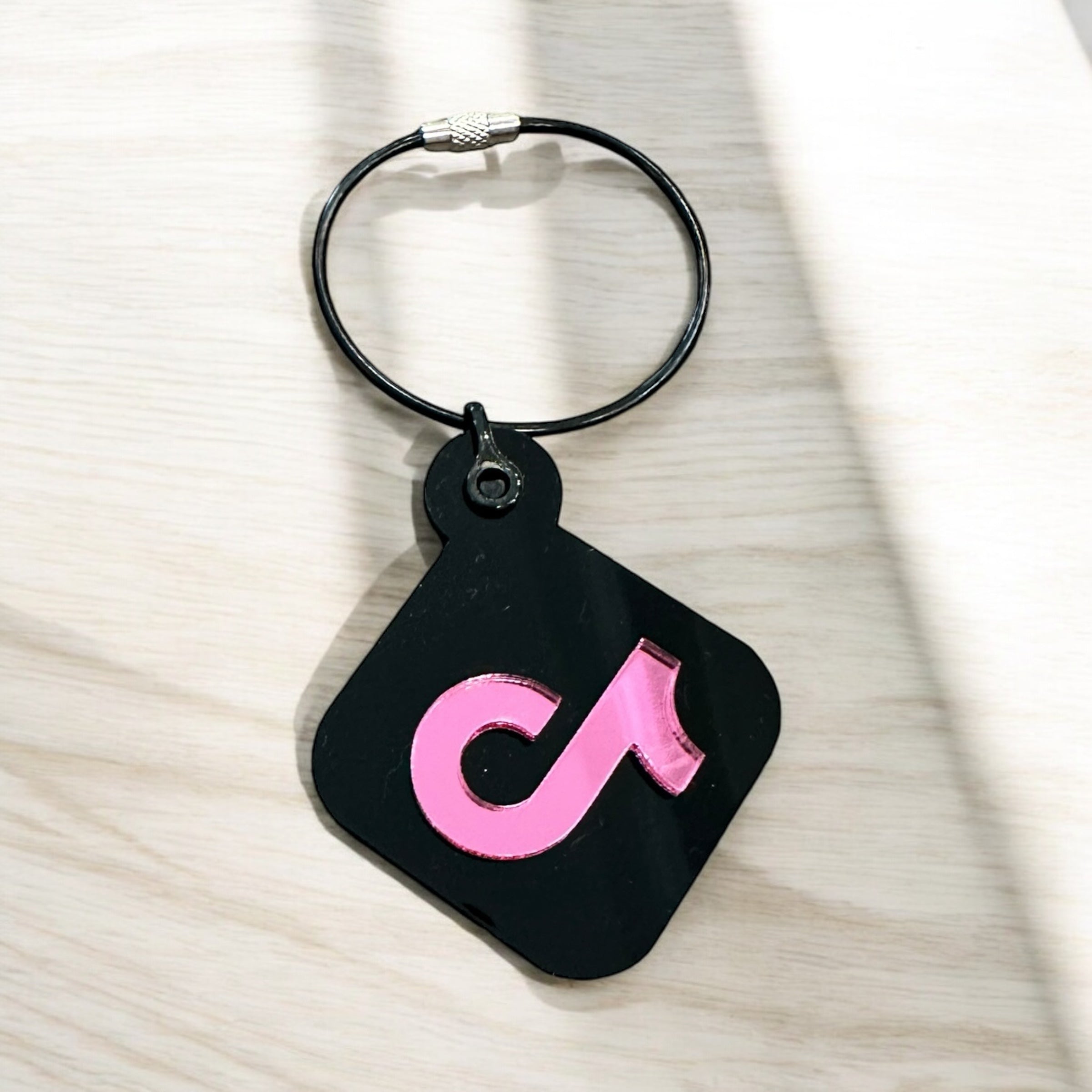 A black keychain with a pink symbol on it, which appears to be a logo or brand symbol.