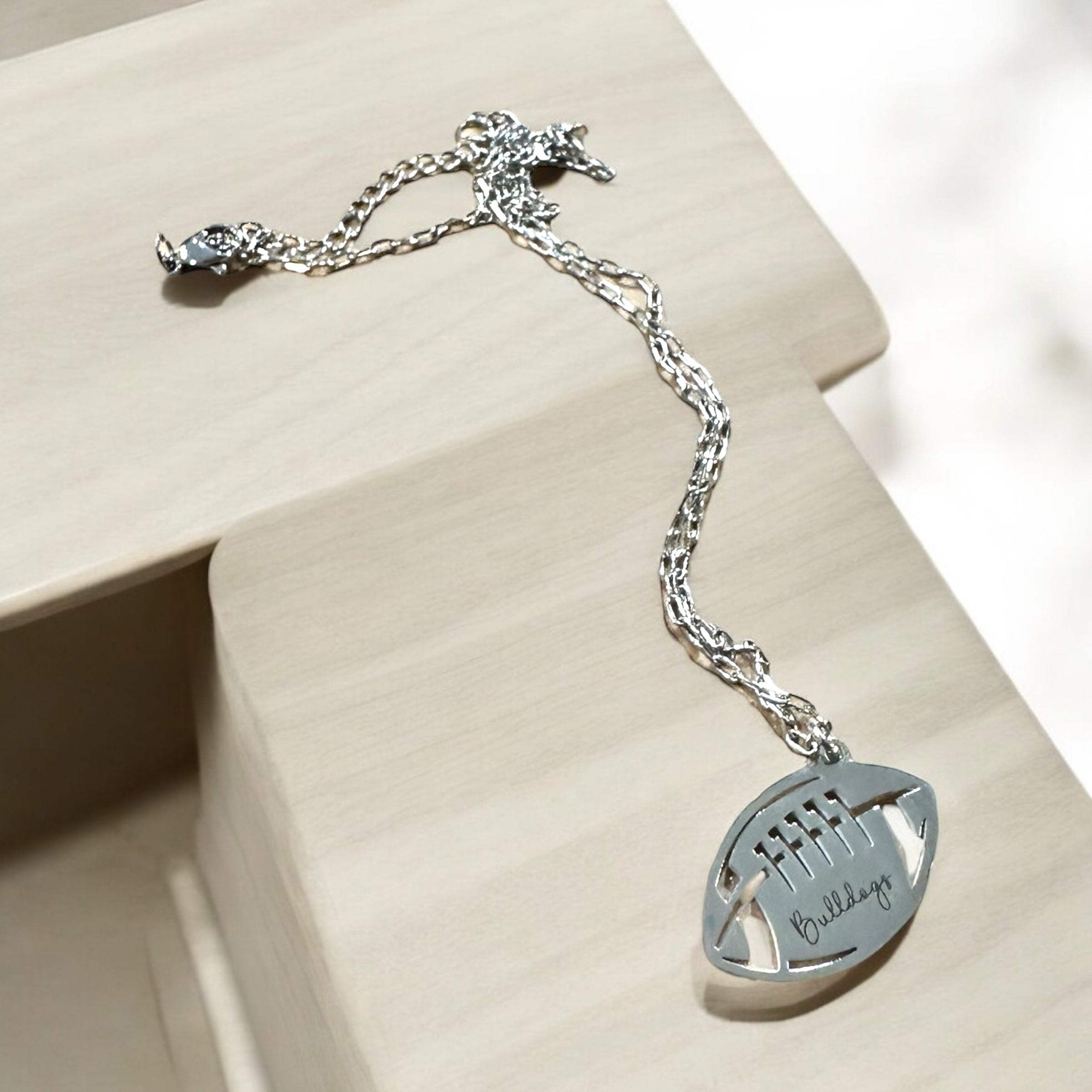 A silver necklace with a pendant in the shape of a football, featuring the word "Bulldogs" engraved on it.