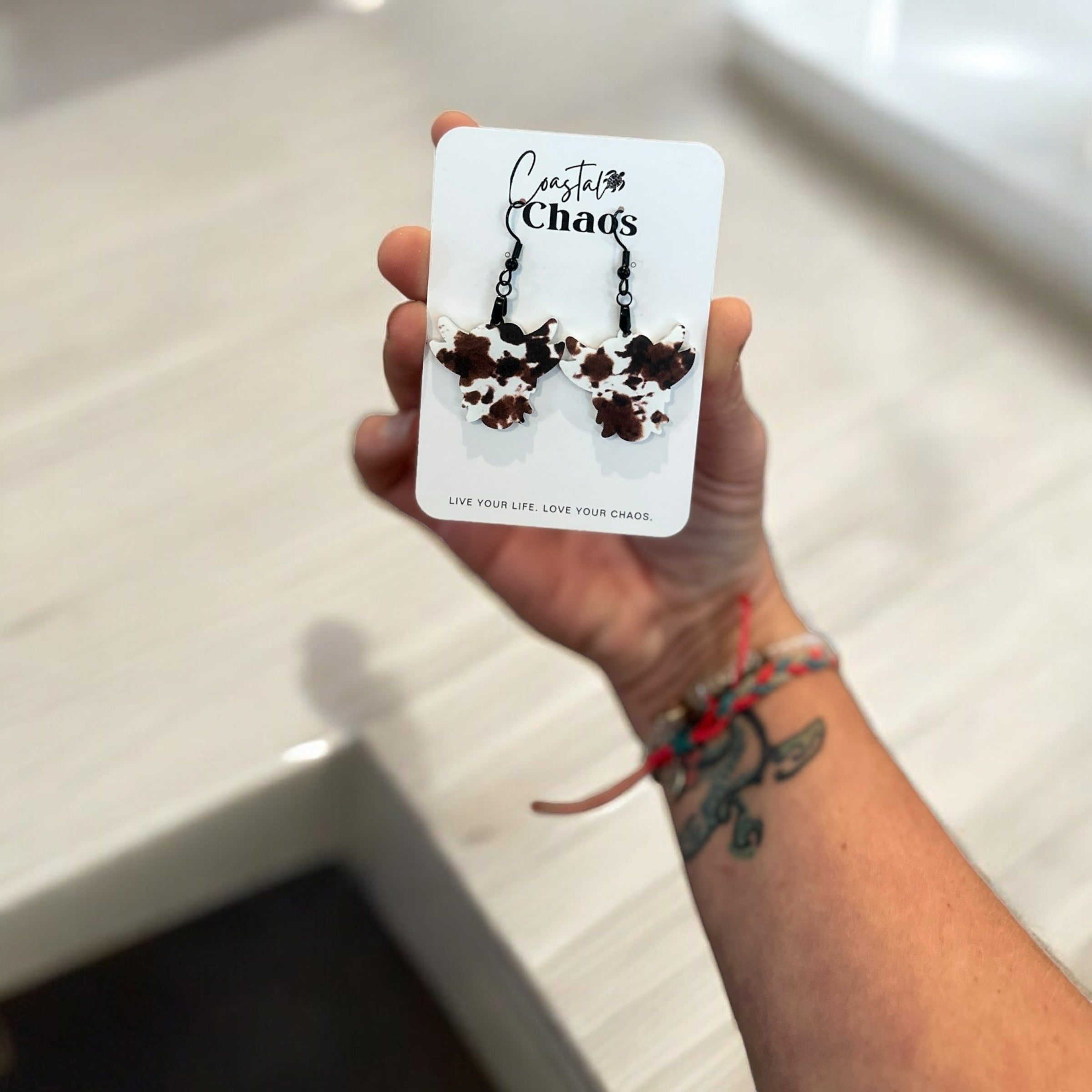 A person is holding a pair of earrings in their hand, which are described as "Chaos" earrings.