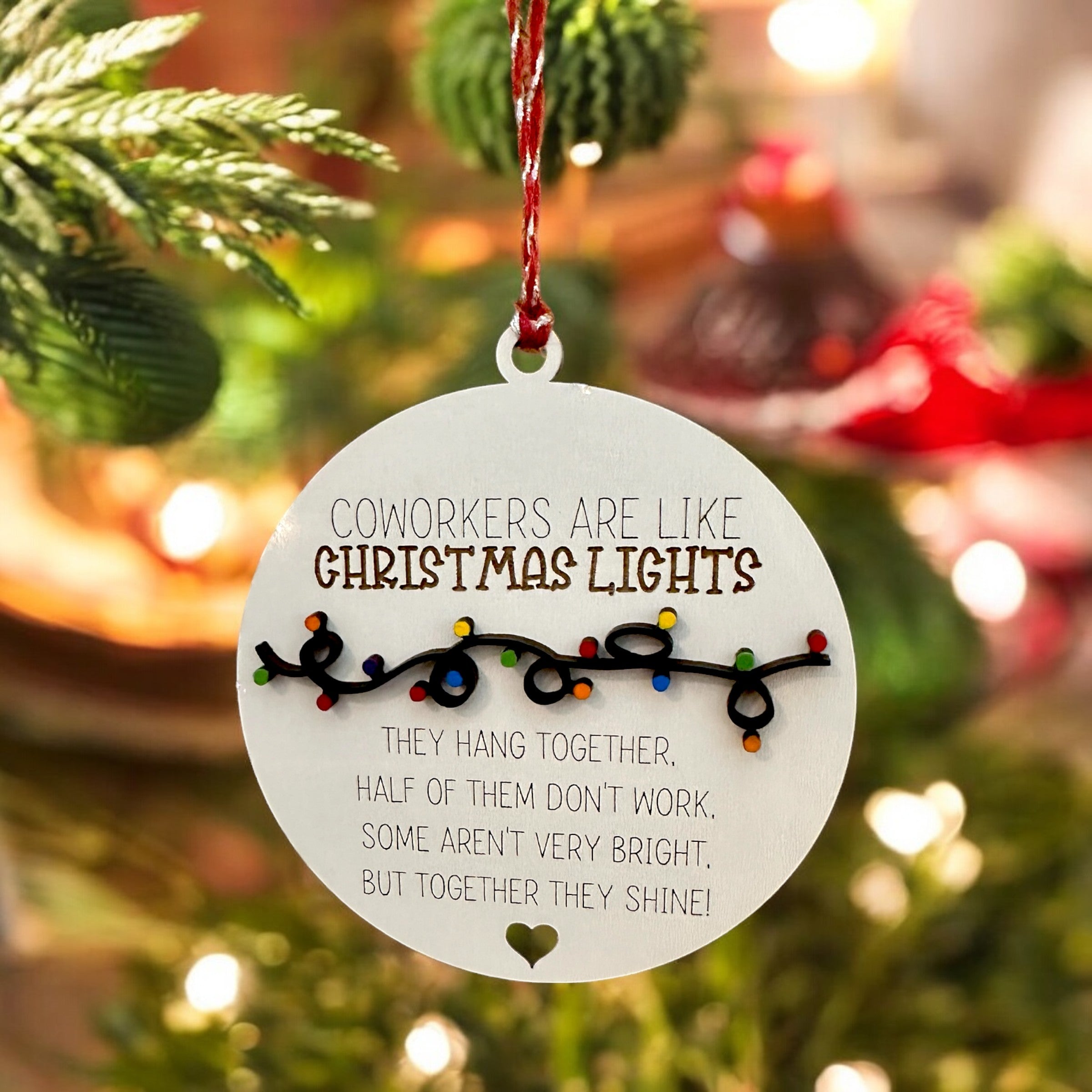 A white ornament with a message about coworkers being like Christmas lights, hanging together and not working half of them, but together they shine.