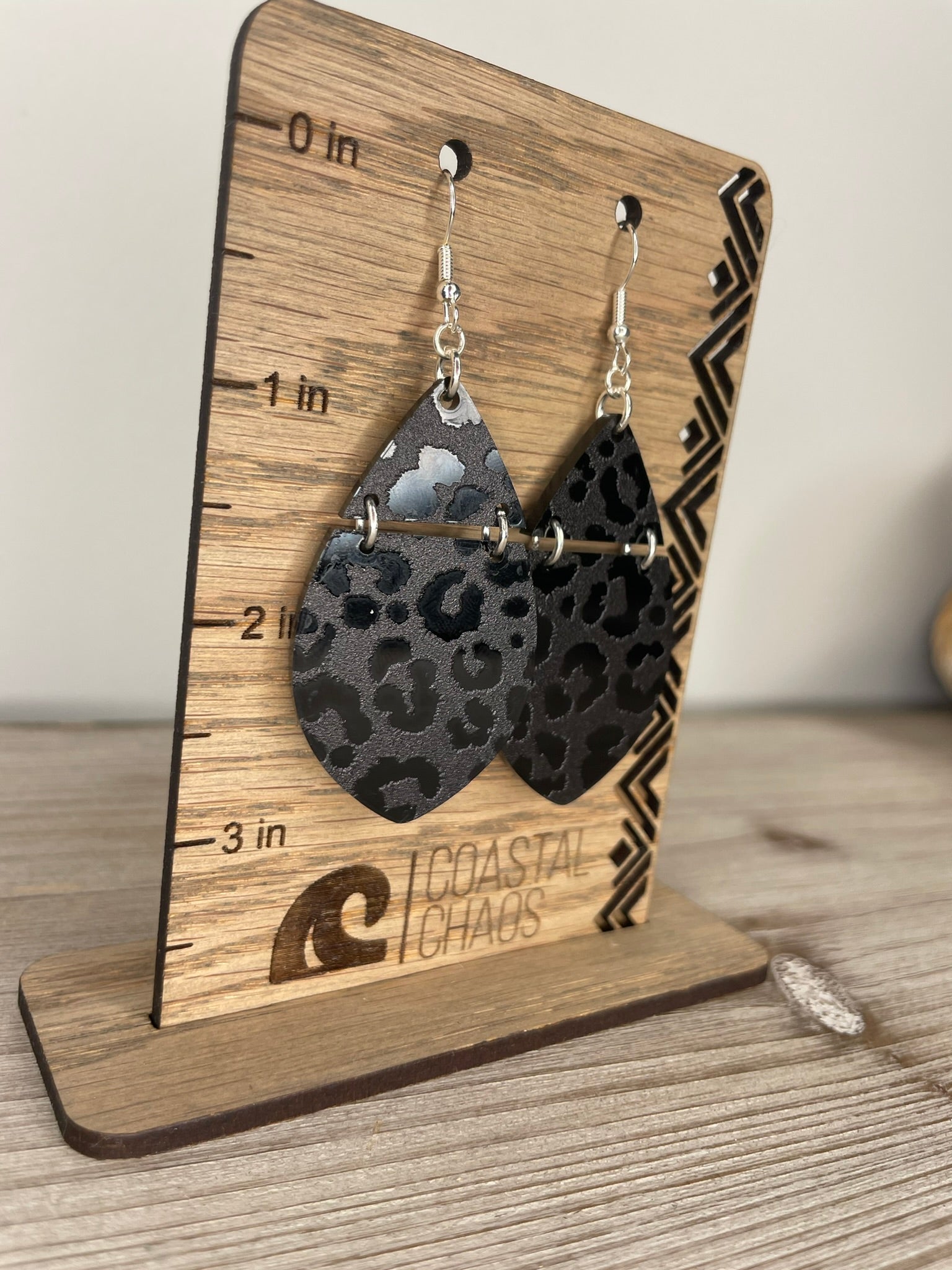 A pair of leopard print earrings displayed on a wooden stand with measurement markings.