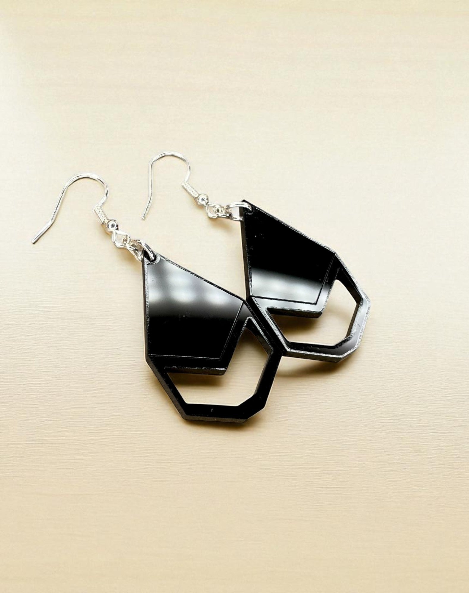 A pair of black geometric earrings with a unique design, resting on a beige background.