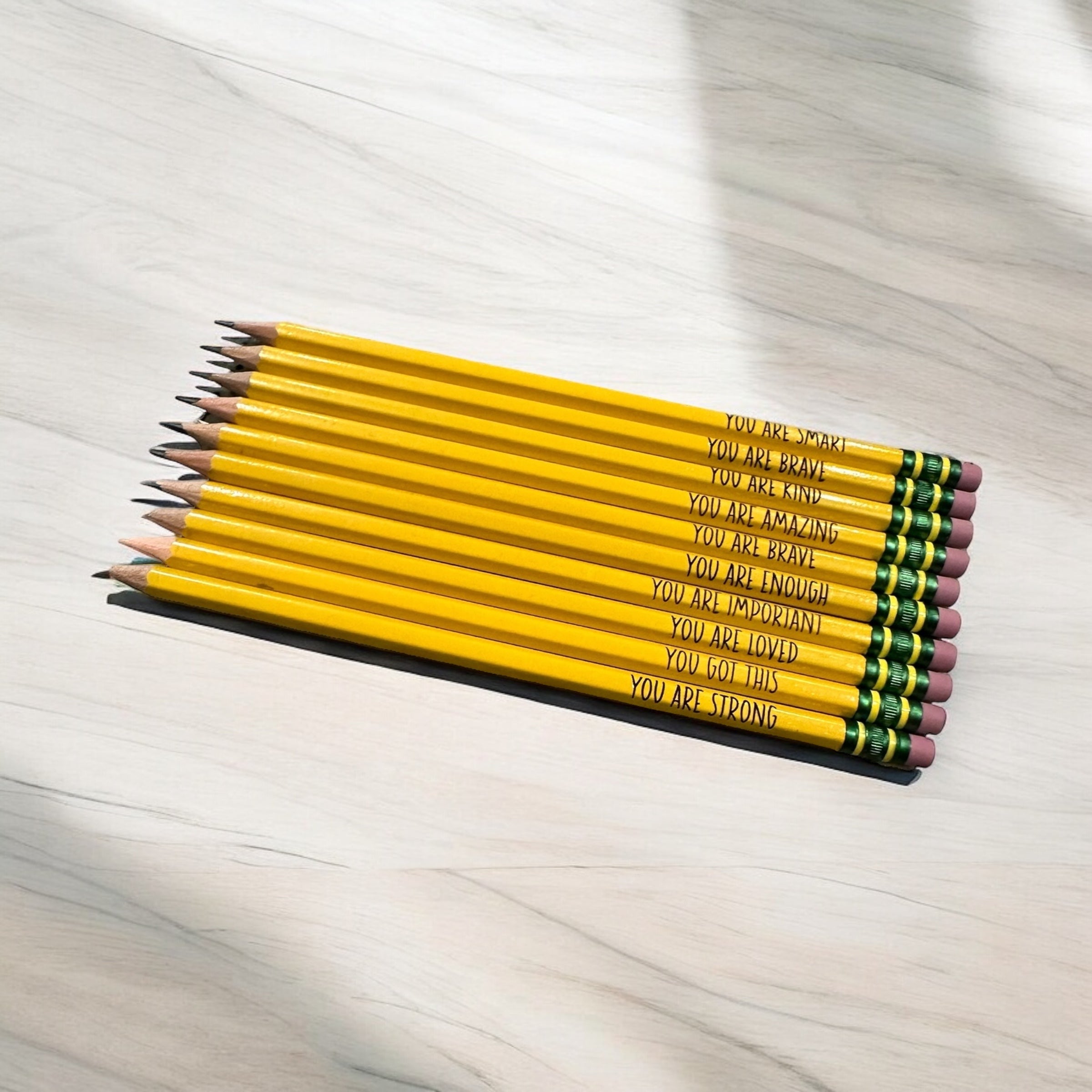 A collection of yellow pencils with motivational messages written on them, arranged in a row on a white surface.
