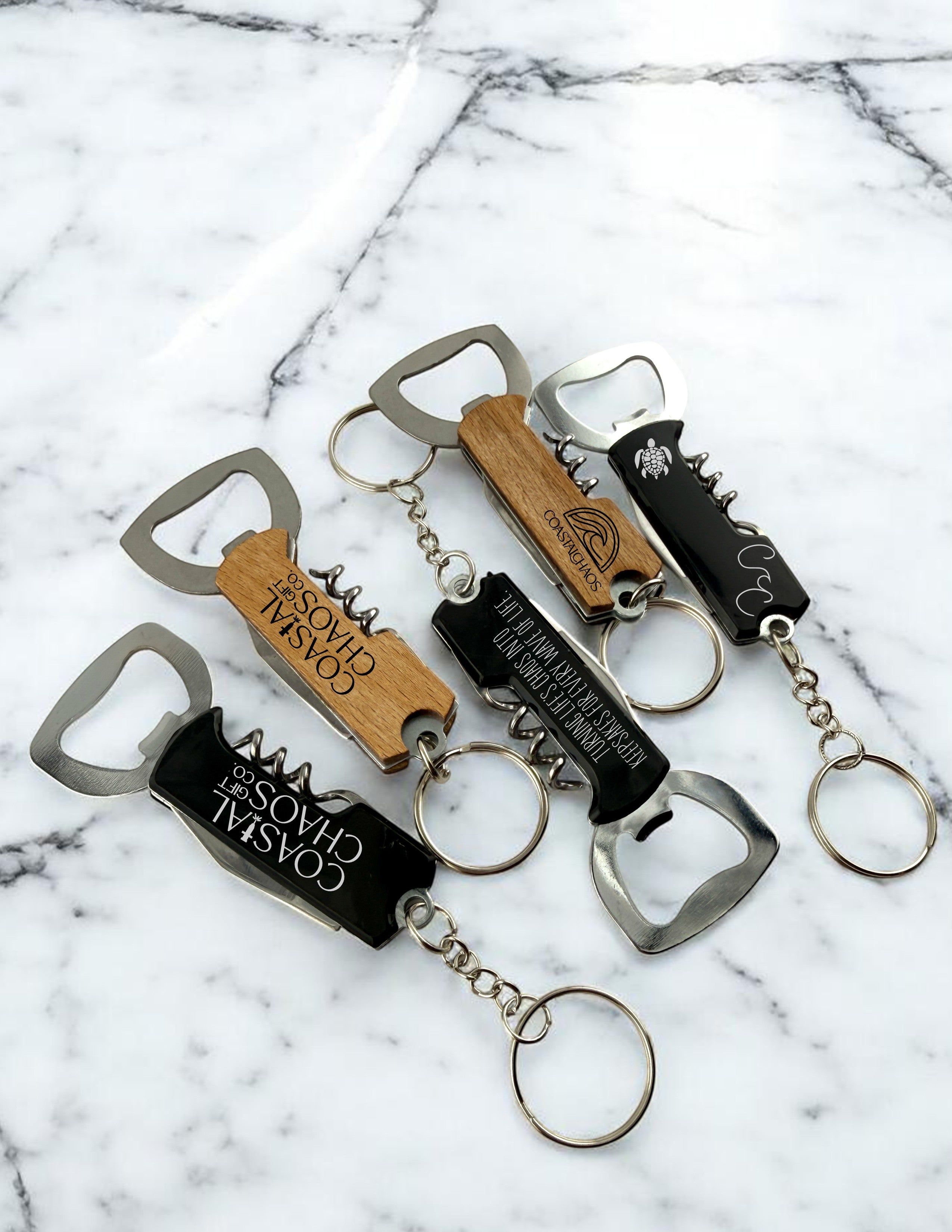 Coastal Chaos Co. multi-tool keychain bottle openers with corkscrews in black and wood finishes, engraved with logos.