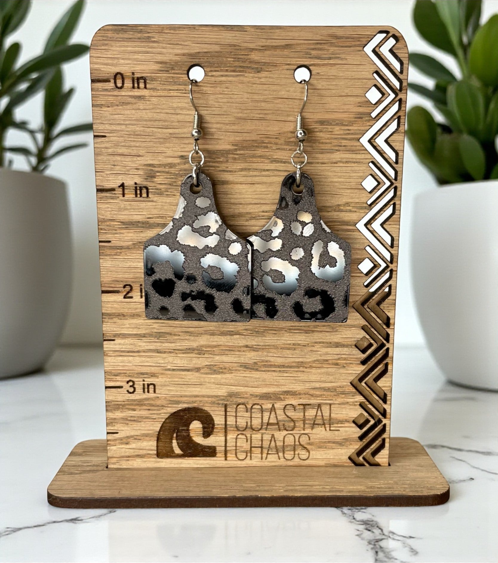 A pair of leopard print earrings displayed on a wooden stand with a scale for size indication.