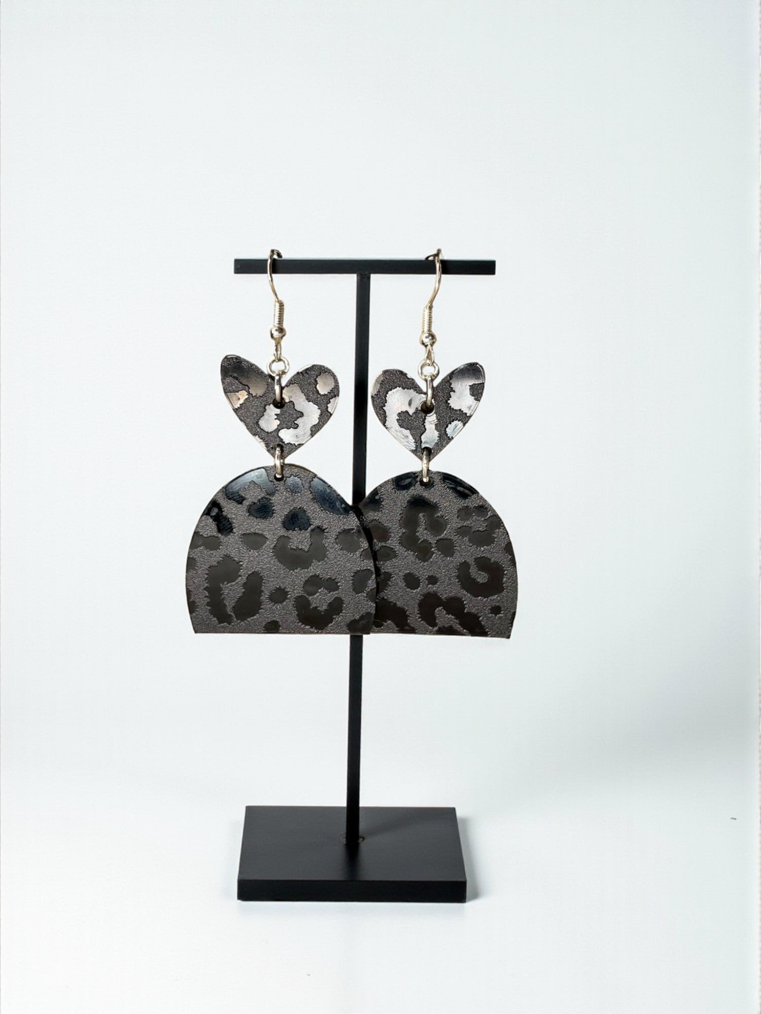 A pair of leopard print earrings displayed on a black stand.