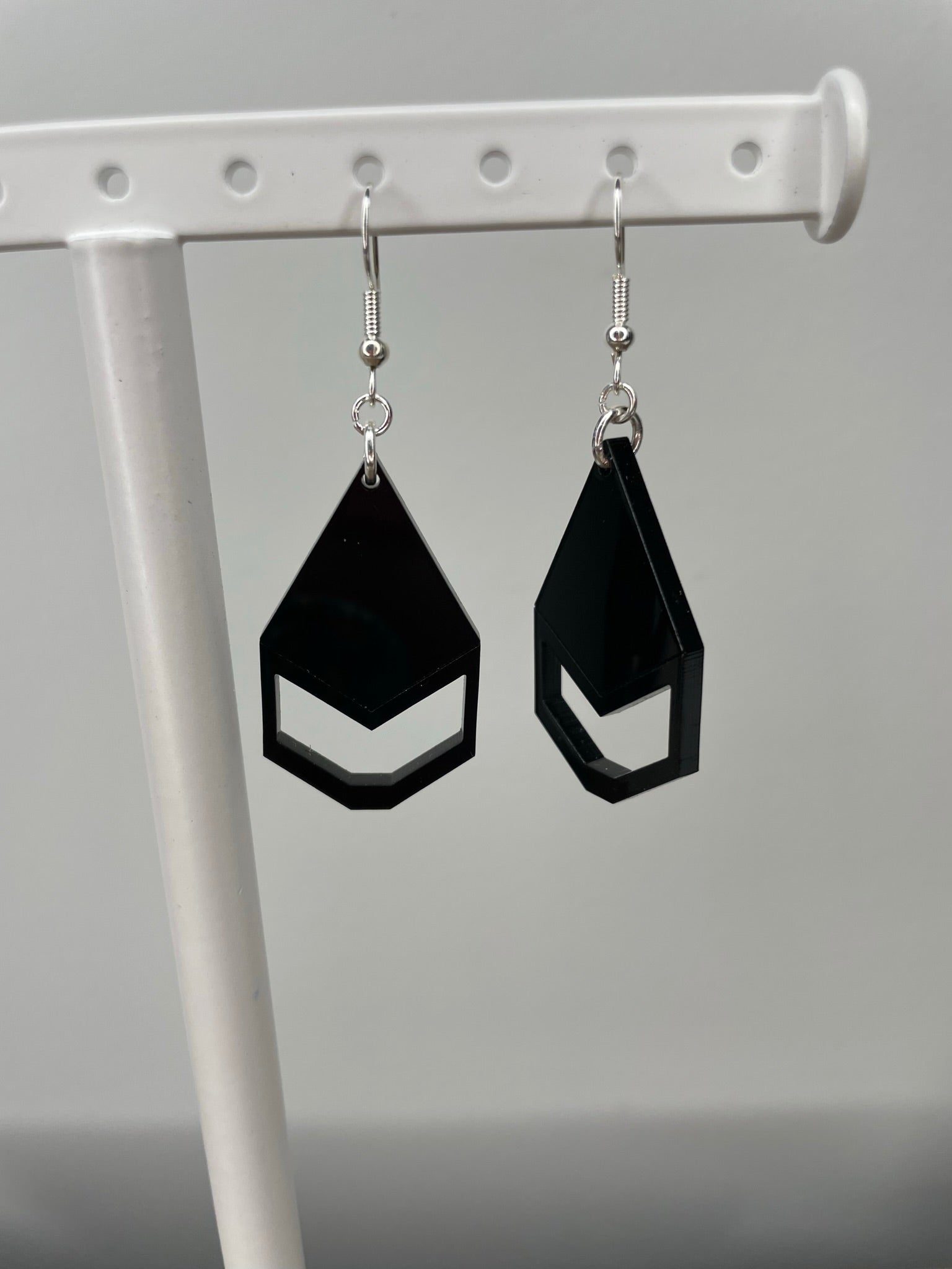 A pair of black geometric earrings hanging from a white metal stand.