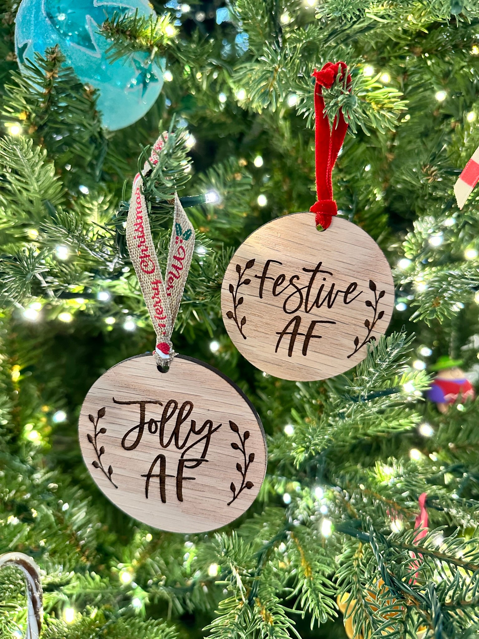 a Christmas tree decorated with two wooden ornaments hanging from the branches. The ornaments have the text "Jolly AF" written on them, indicating a humorous or playful message.