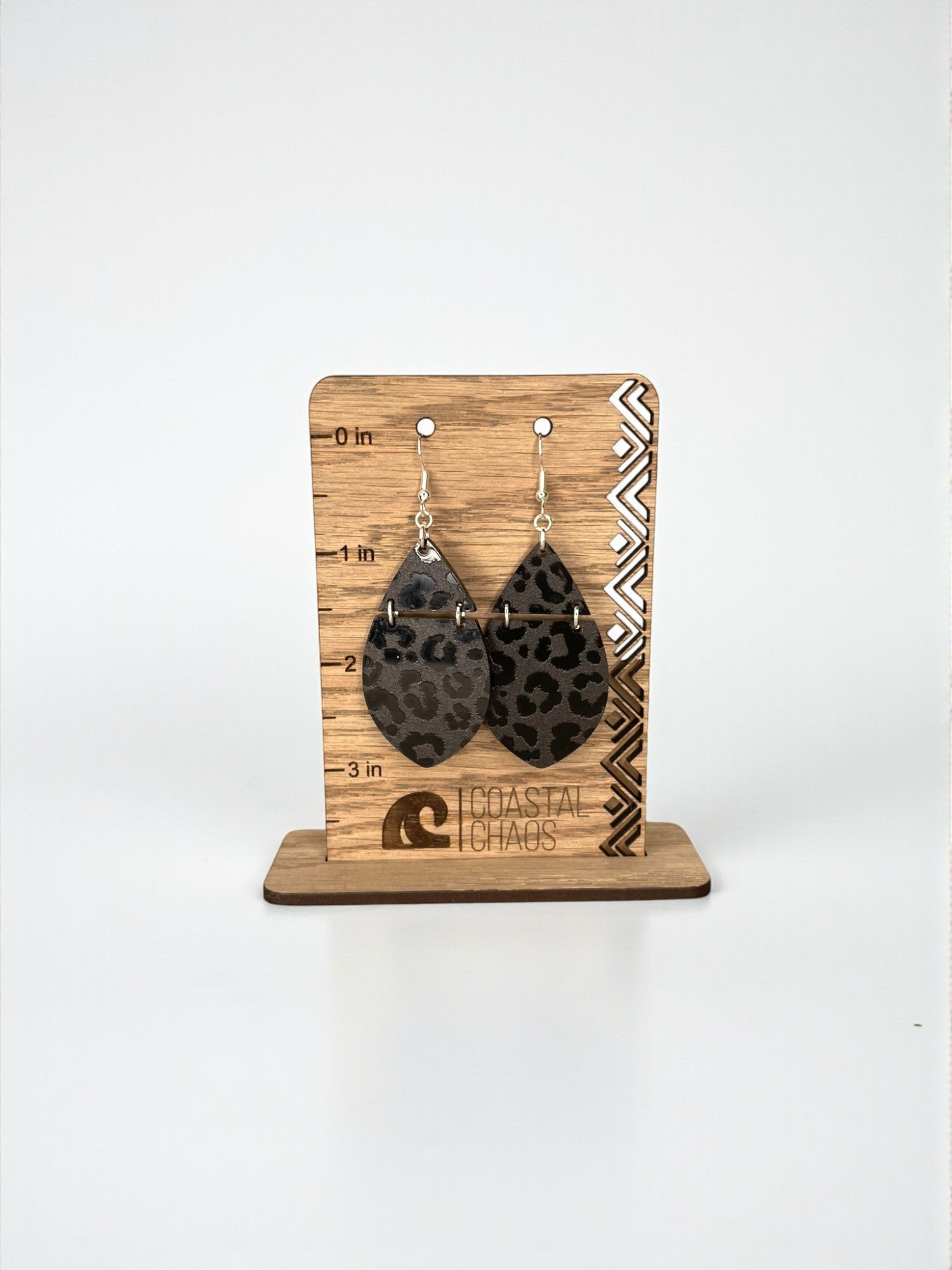 A pair of leopard print earrings displayed on a wooden stand.
