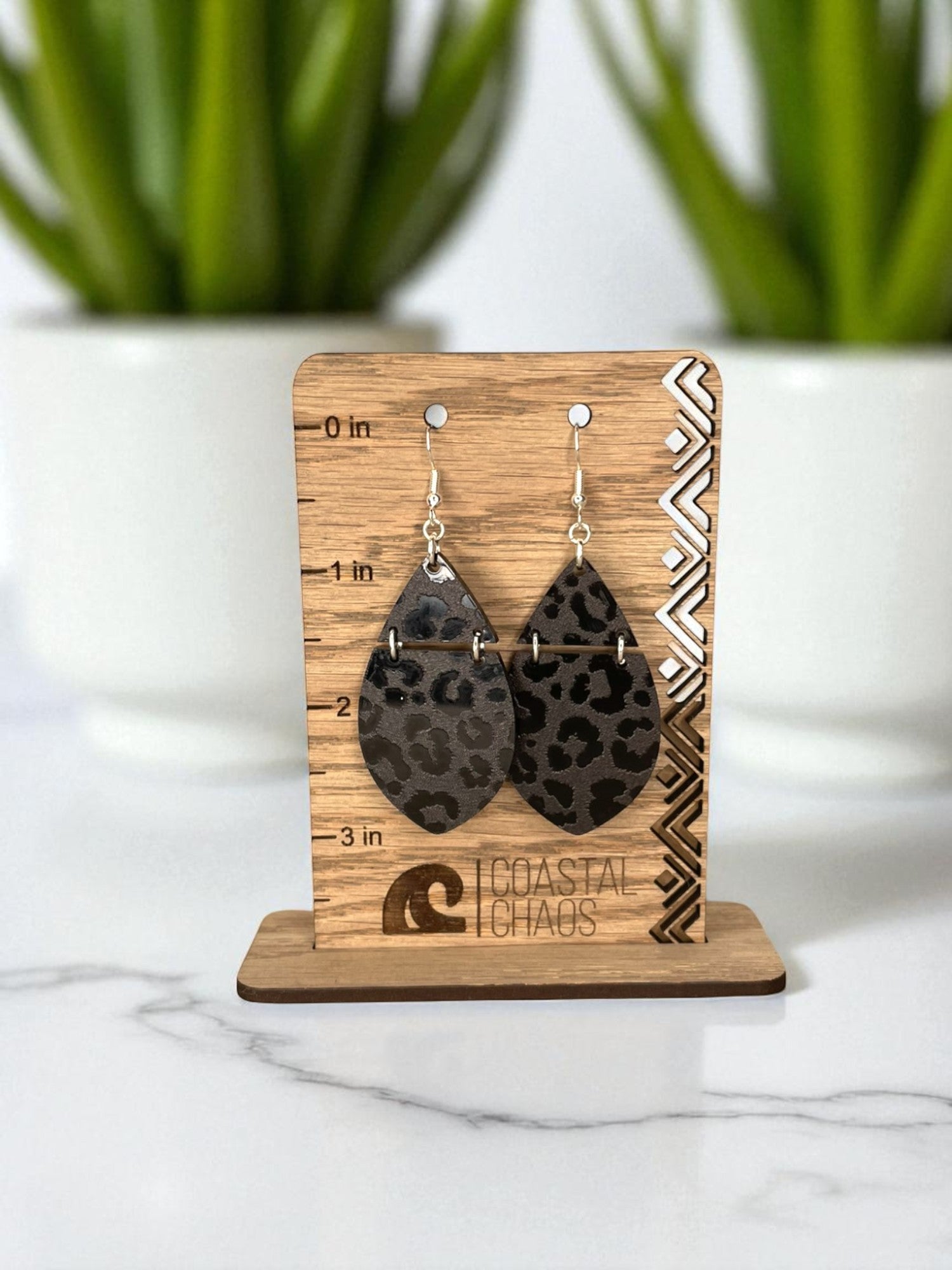 A pair of leopard print earrings displayed on a wooden stand, with a ruler for size reference.