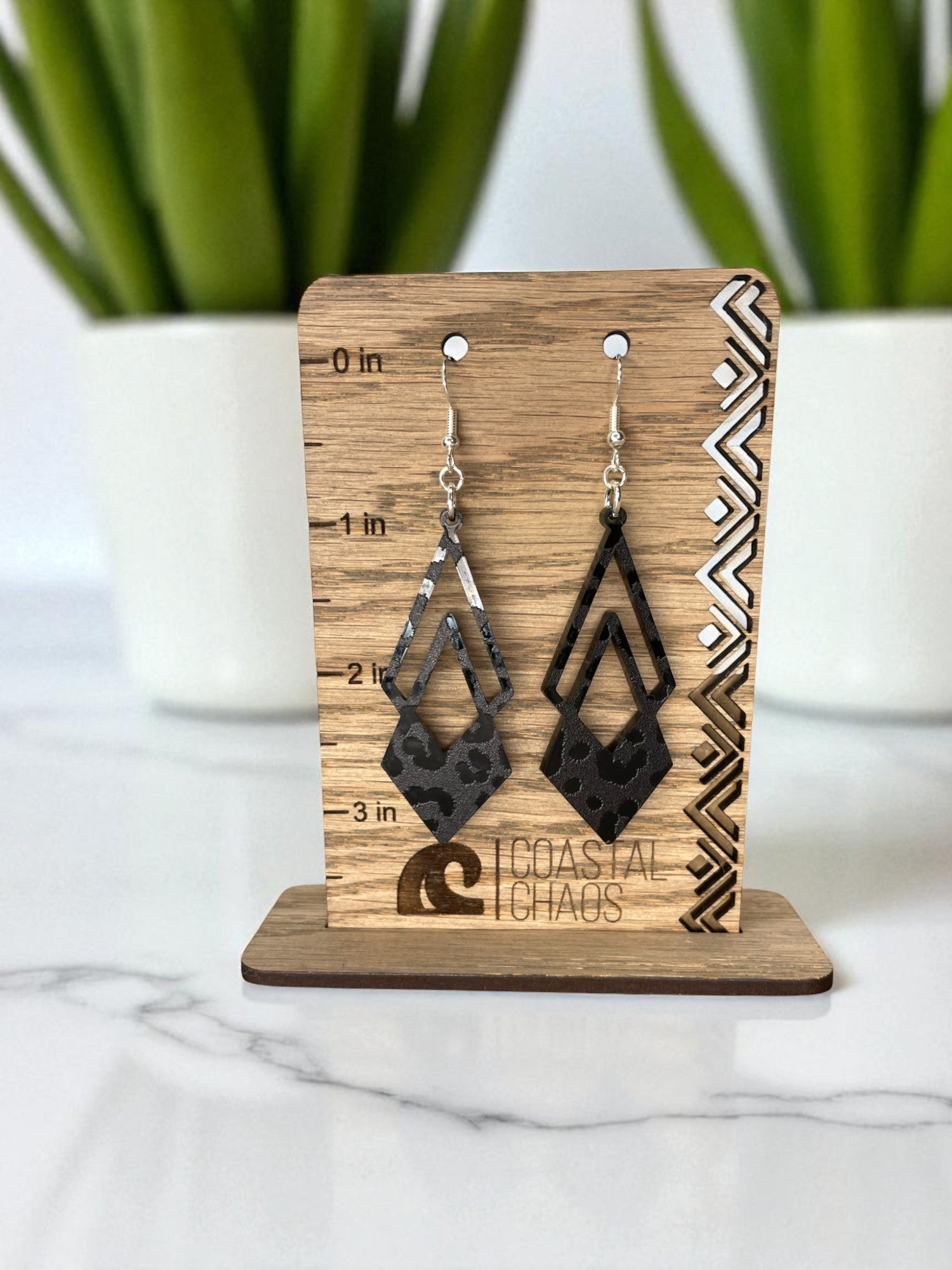 A pair of earrings on a wooden stand, with a ruler for size indication.