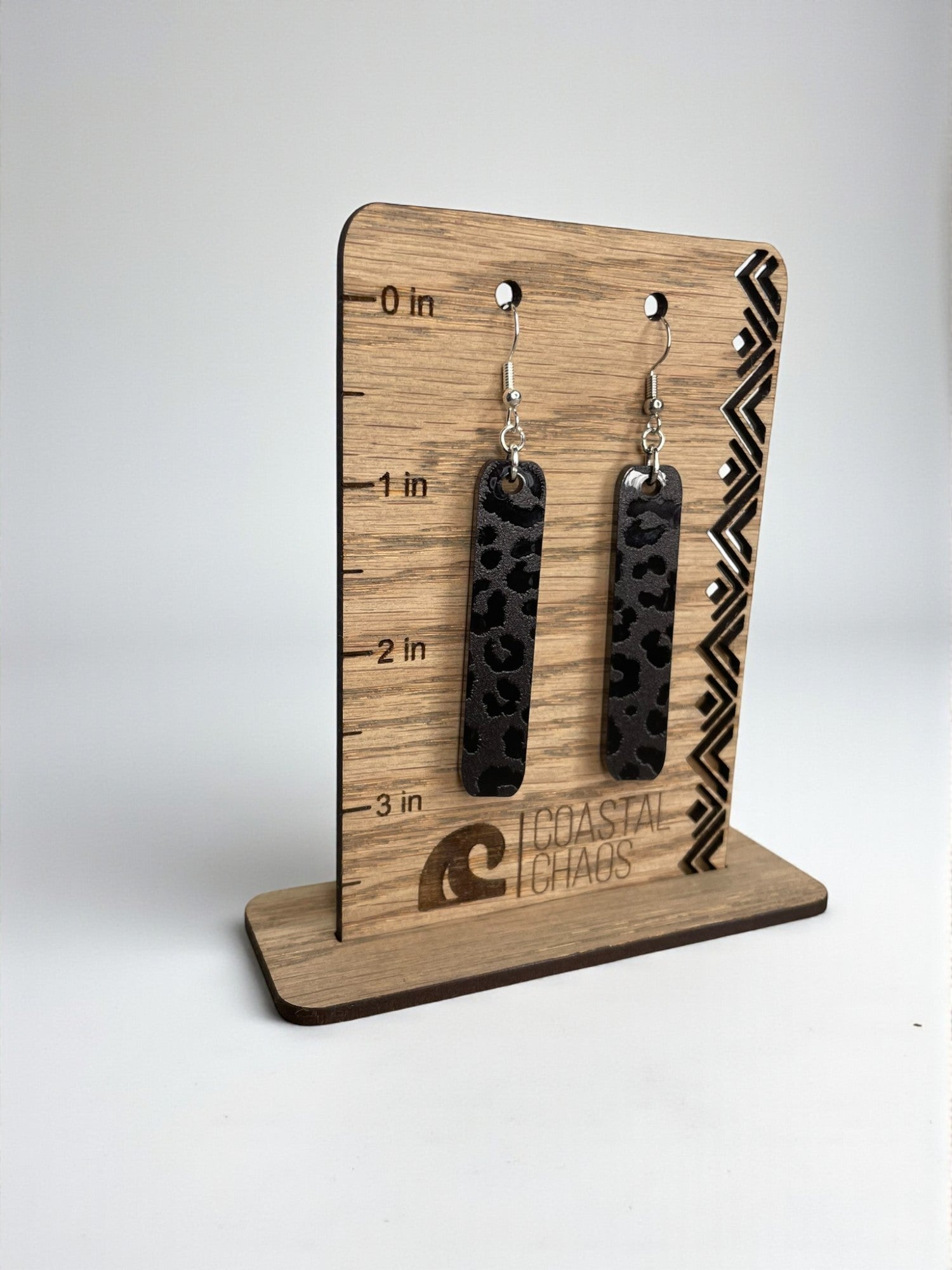 A pair of black leopard print earrings displayed on a wooden stand with measurement markings.