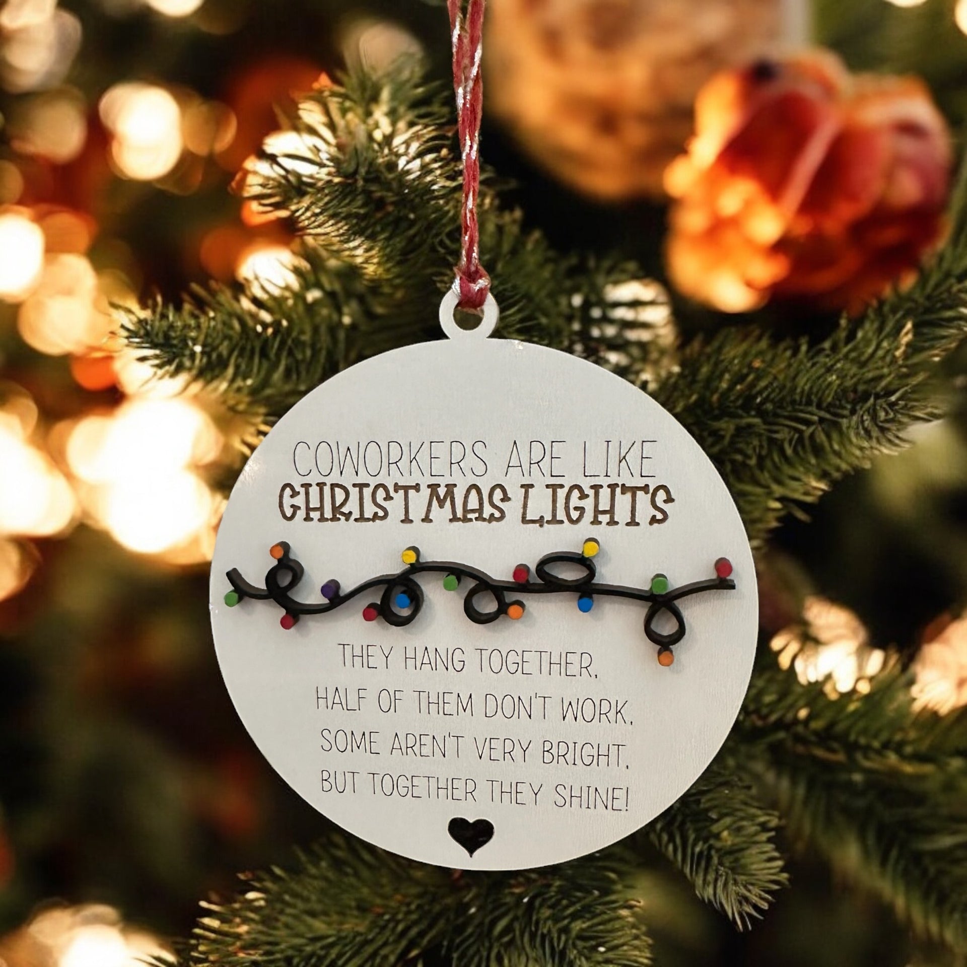 A round ornament hanging on a Christmas tree, with a message about coworkers being like Christmas lights.