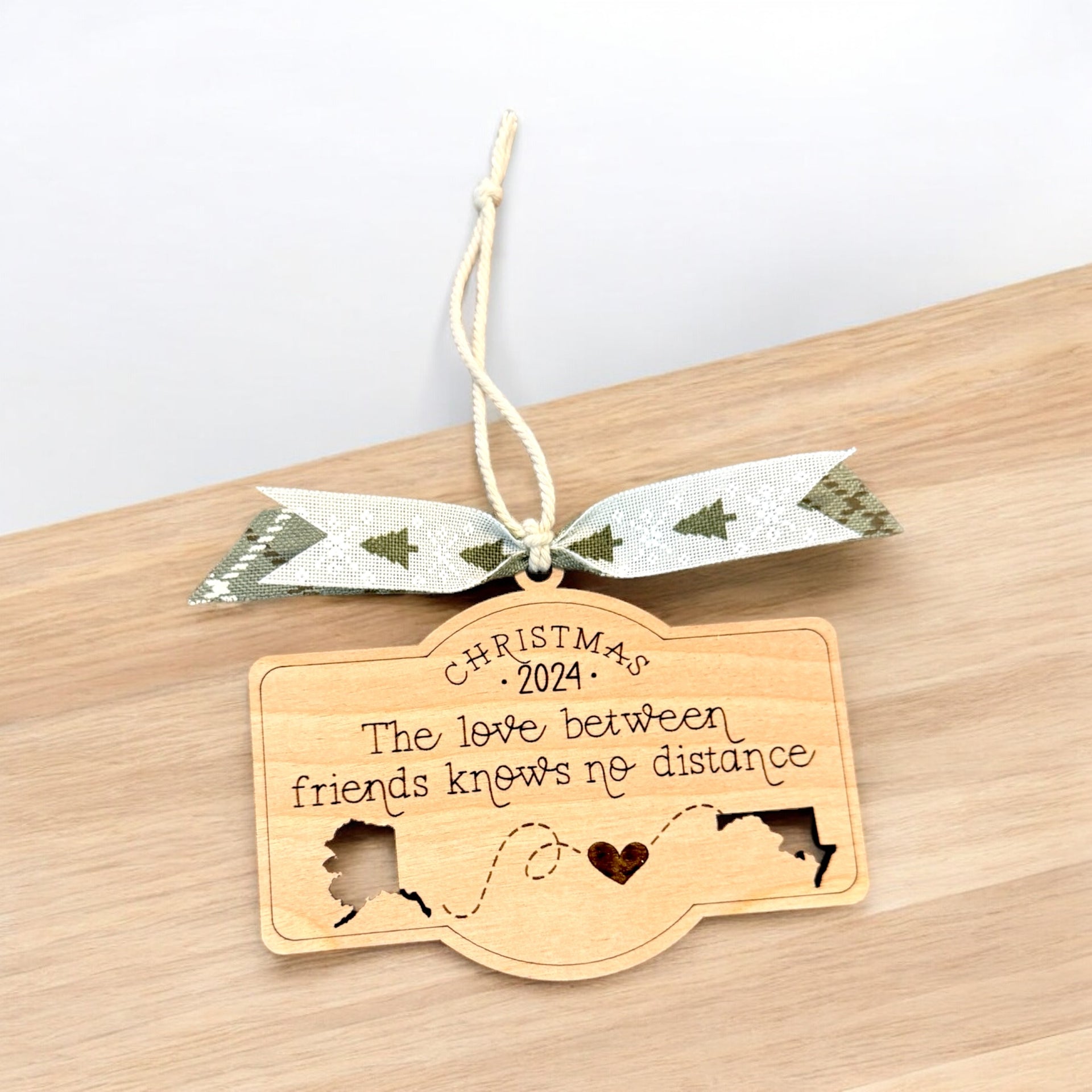 A wooden ornament with a ribbon and a message about the love between friends, hanging on a wooden surface.