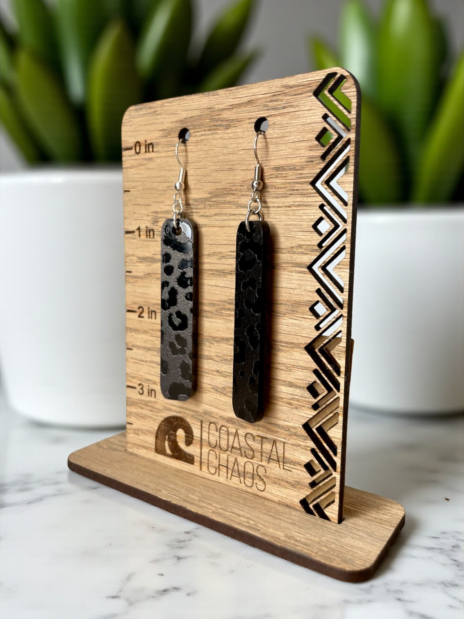 A pair of black leopard print earrings displayed on a wooden stand with a ruler for size reference.