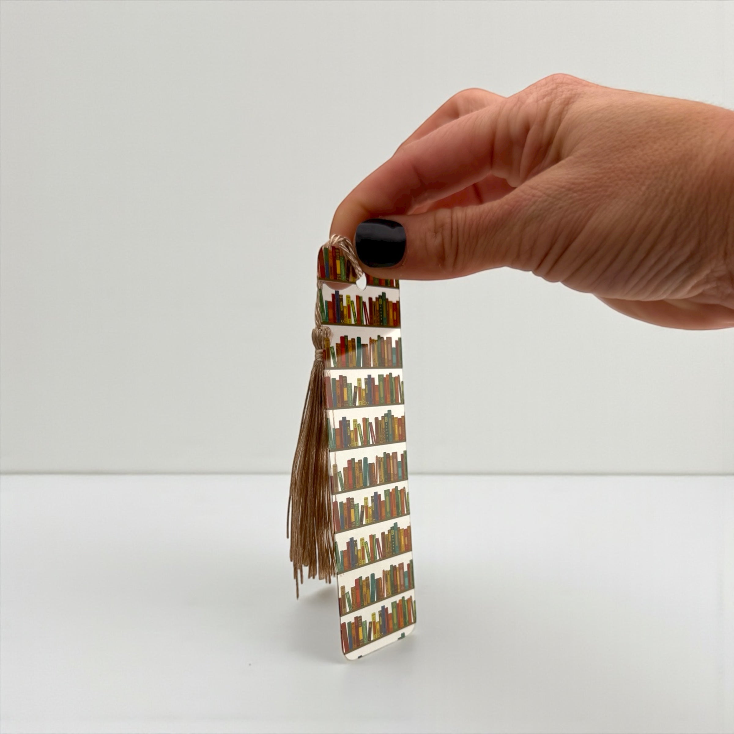 A hand holding a small, colorful book-themed bookmark with a tassel attached.