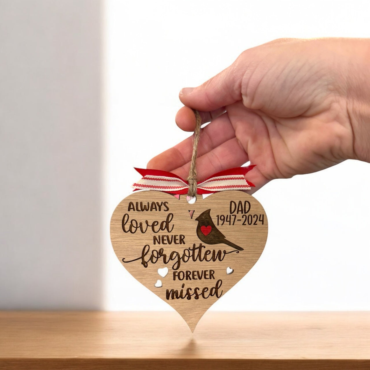 A hand holding a wooden heart-shaped ornament with a ribbon and a message about a father.