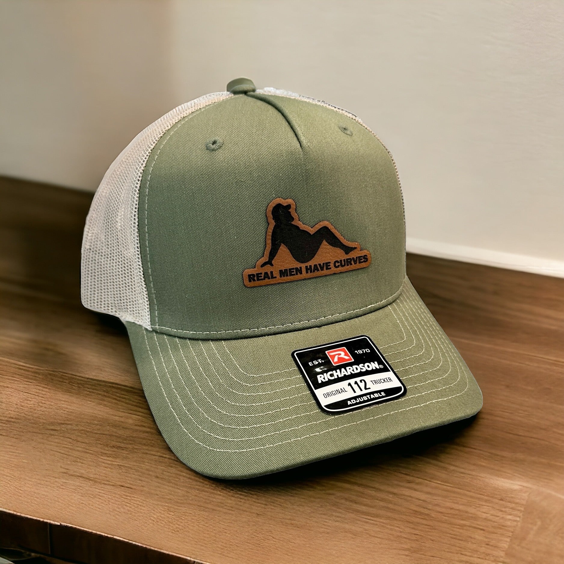 A green baseball cap with a patch that says "Real men have curves" and a logo of a person sitting on a skateboard.