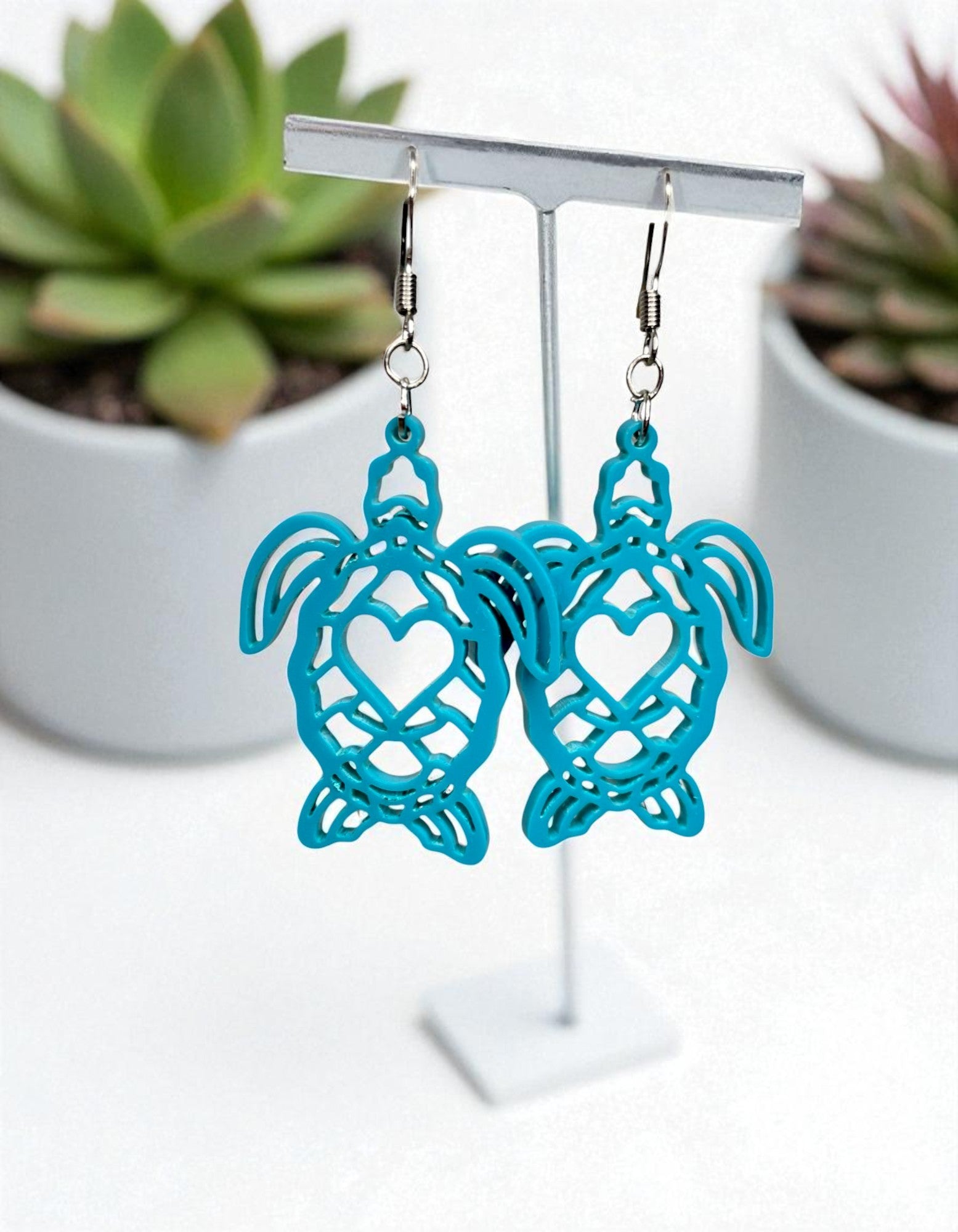 A pair of turquoise earrings with a heart-shaped cutout design, displayed on a white stand.