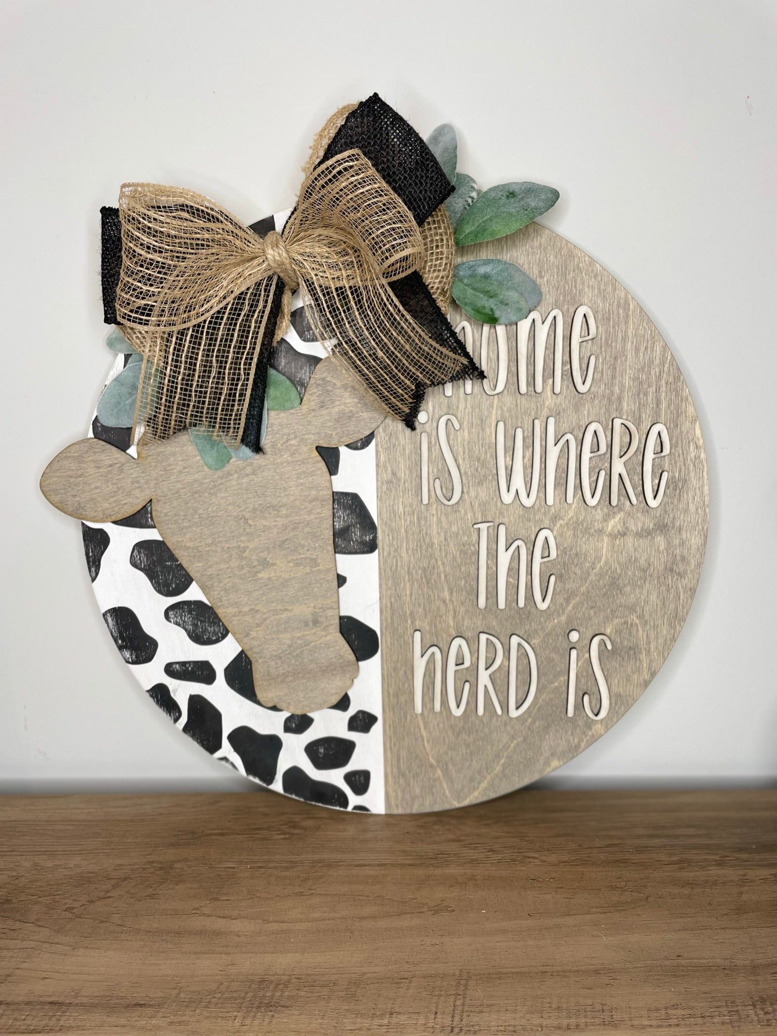 A wooden sign with a cow silhouette and a decorative bow, along with the text "Home is where the nerd is" written on it.