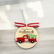 A wooden ornament with a red truck and a Christmas tree, hanging on a white surface.