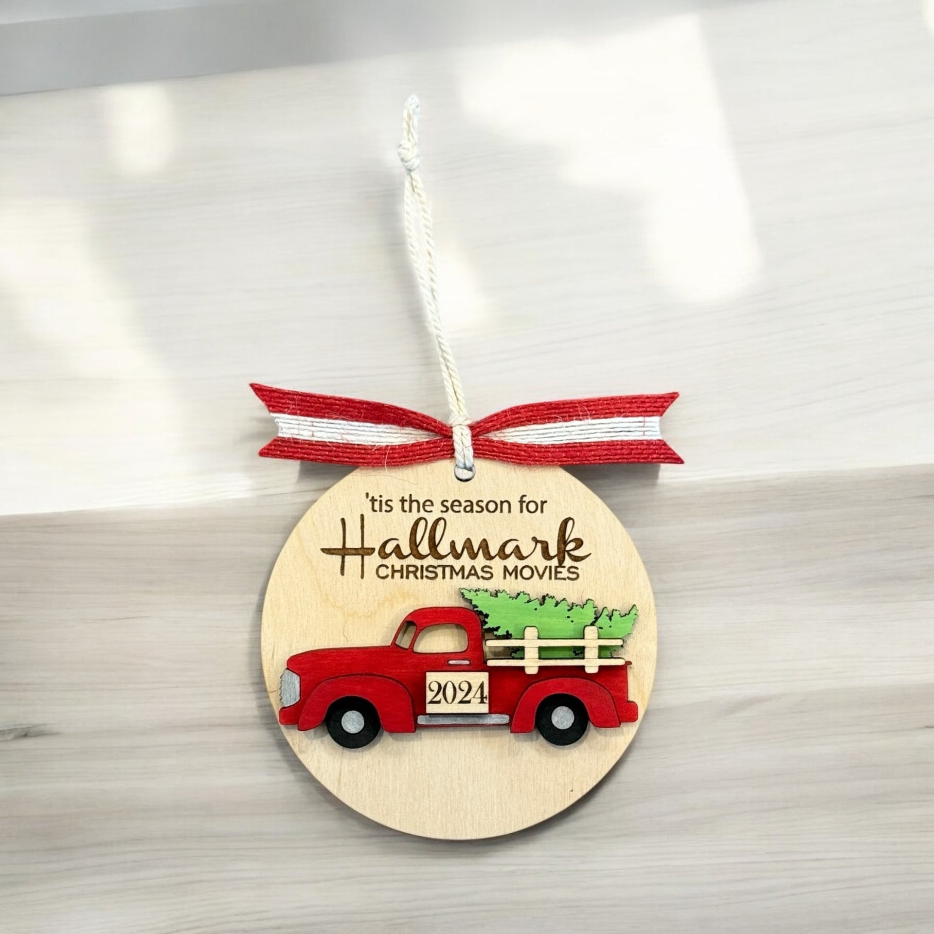 A wooden ornament with a red truck and a Christmas tree, hanging on a white surface.