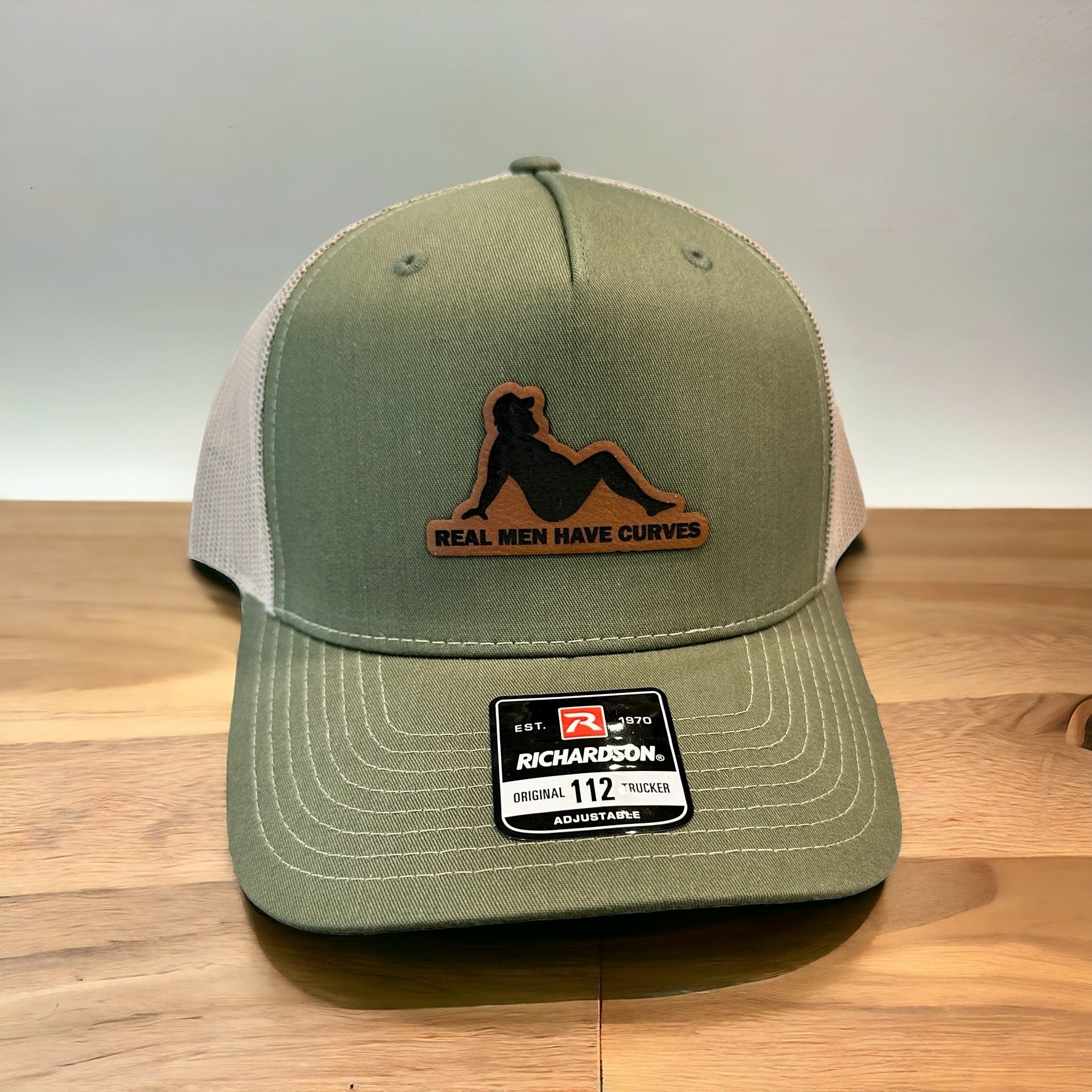 A green baseball cap with a patch on the front that says "Real men have curves".