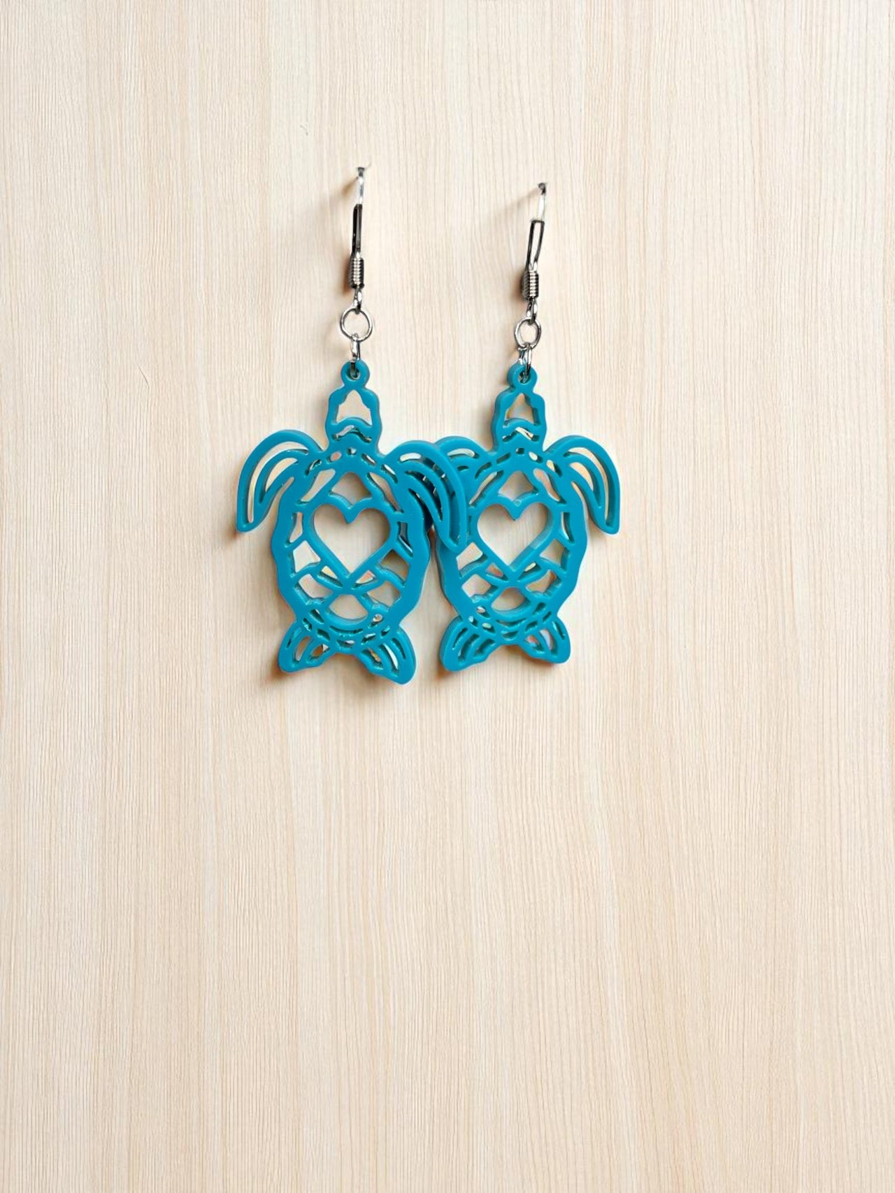 A pair of blue earrings with heart-shaped cutouts, hanging on a wooden surface.