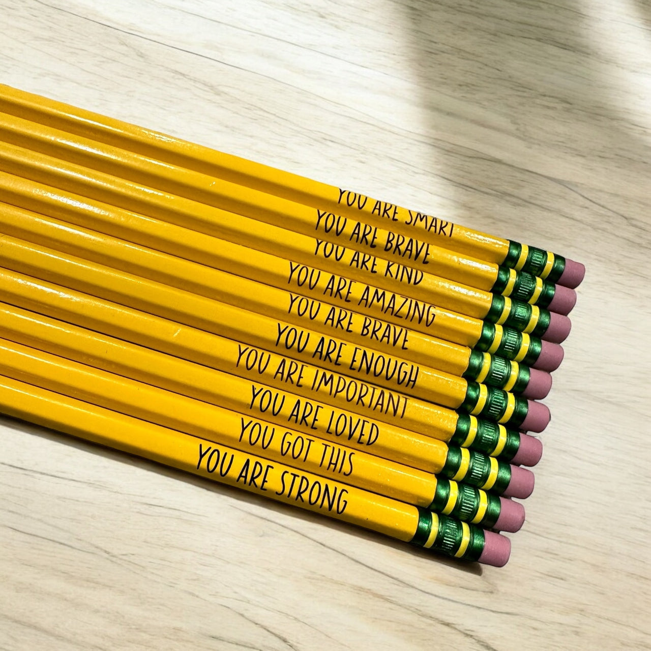 A row of yellow pencils with motivational messages written on them, placed on a wooden surface.