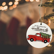 A round ornament hanging from a Christmas tree, featuring a red truck carrying a Christmas tree.