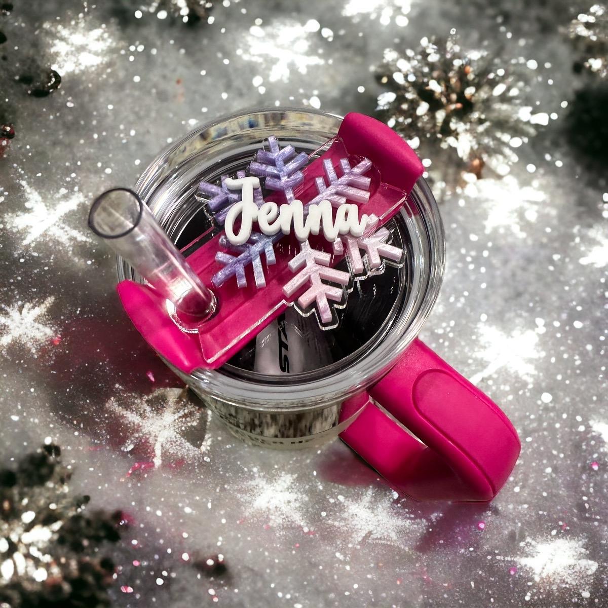 A pink cup handle with a snowflake-shaped decoration is placed on a snowy surface, surrounded by sparkling snowflakes.