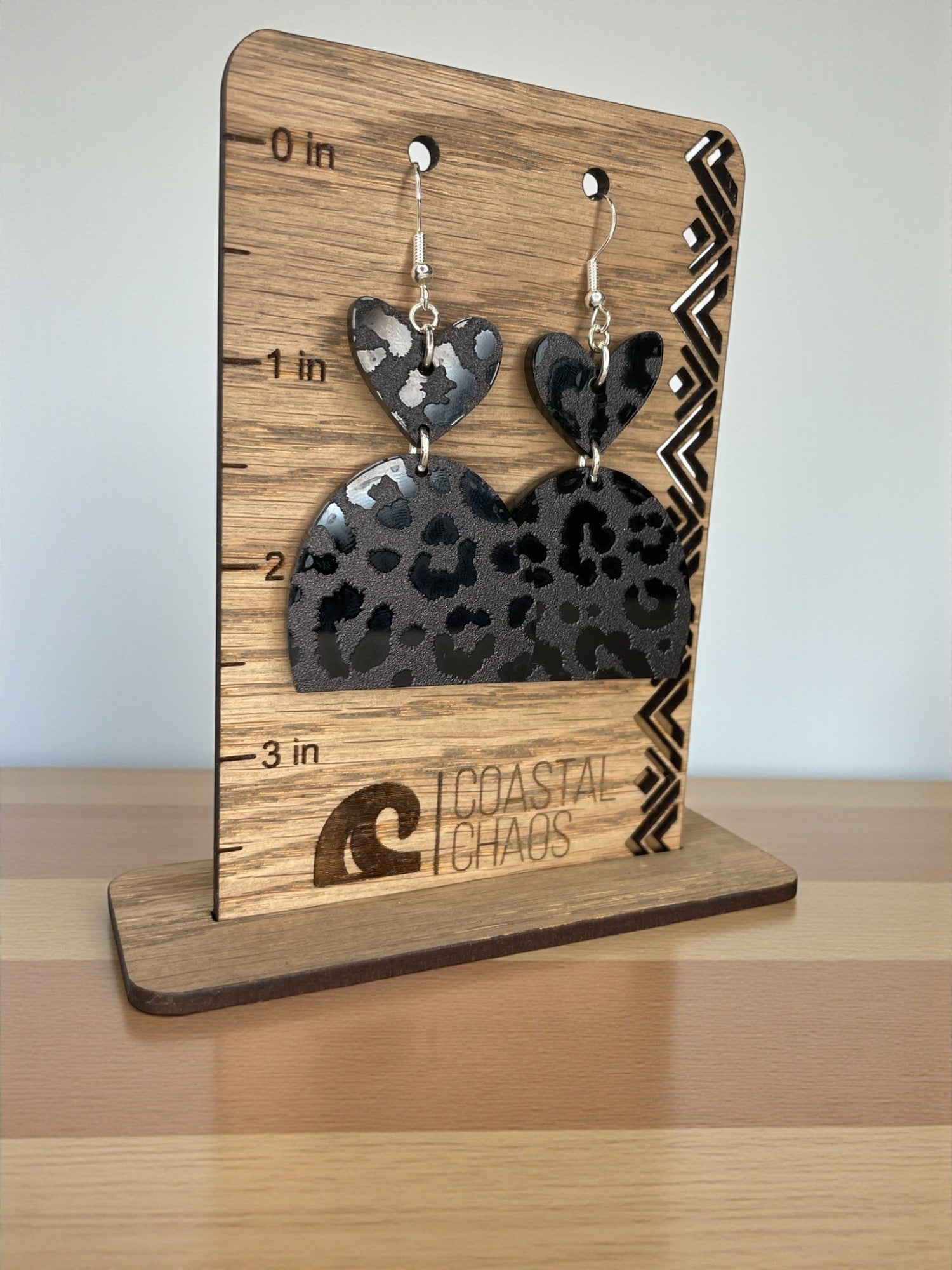 A pair of leopard print earrings displayed on a wooden stand with a ruler for size reference.