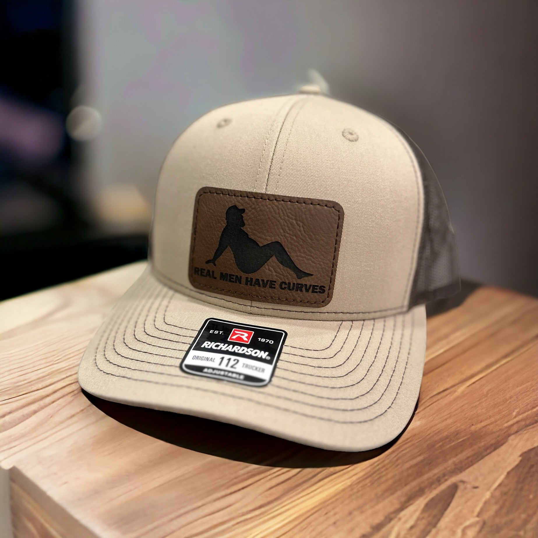 A tan baseball cap with a black logo and text on it, placed on a wooden surface.