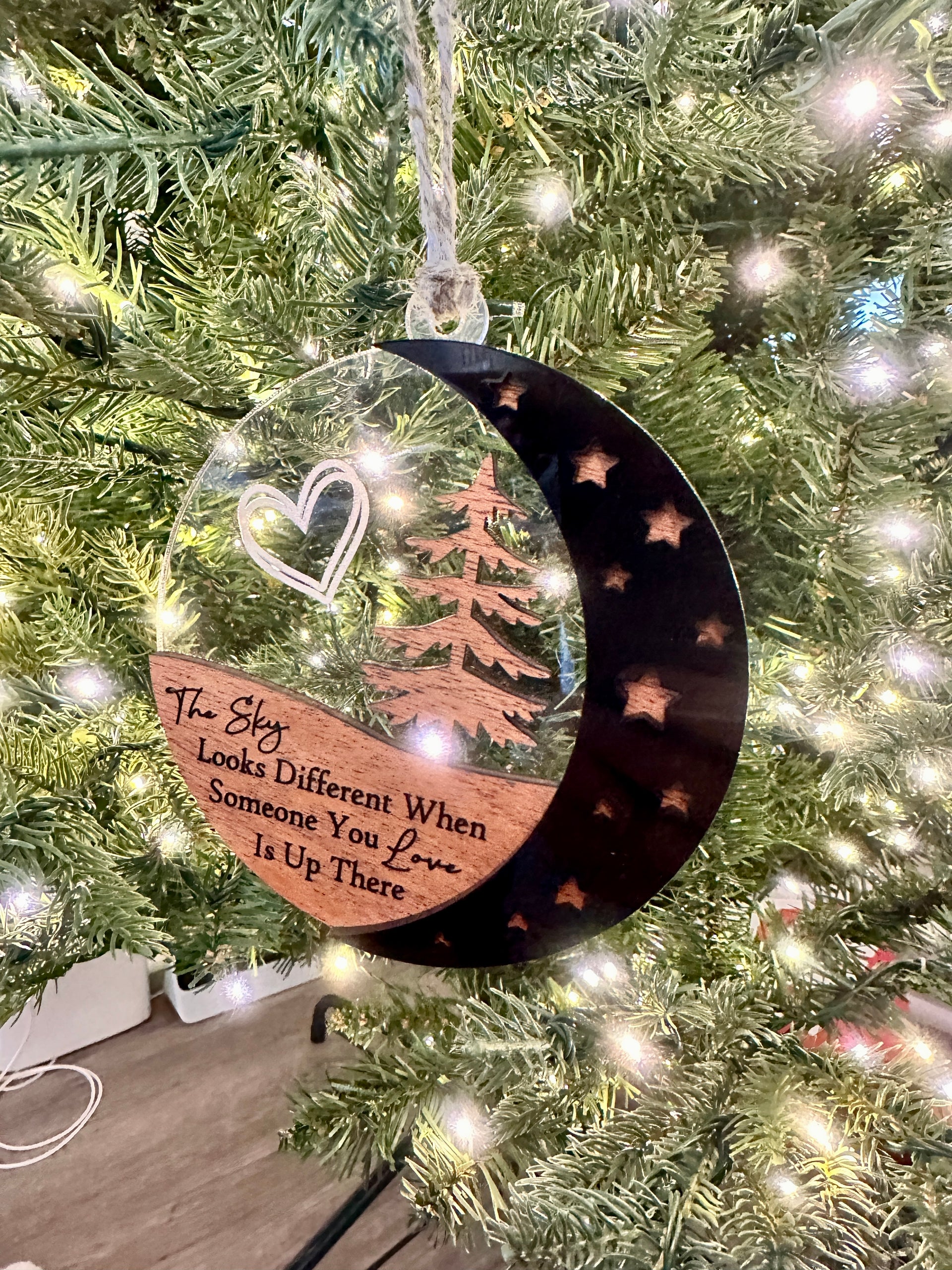 A clear ornament with a crescent moon and stars hanging from a Christmas tree.