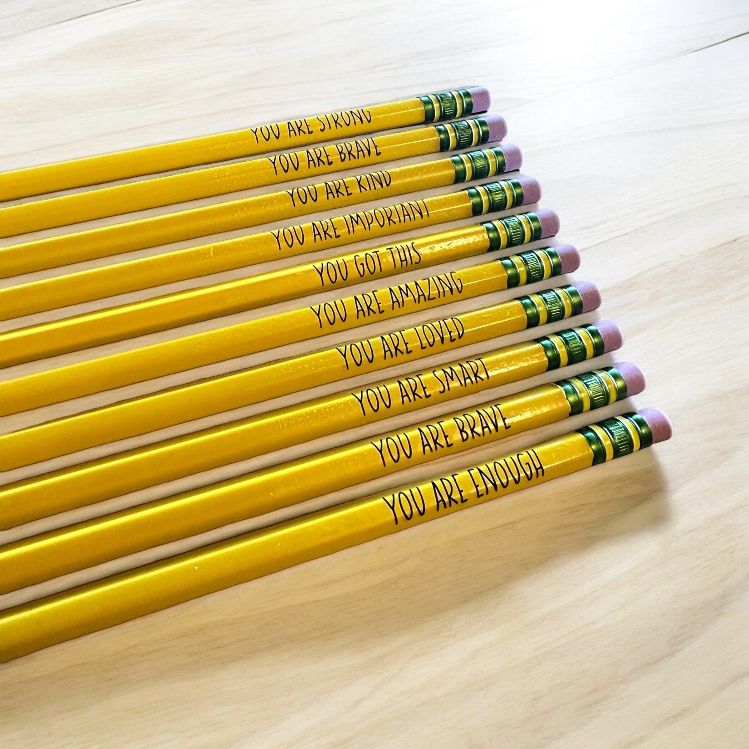A row of yellow pencils with positive messages written on them, placed on a wooden surface.