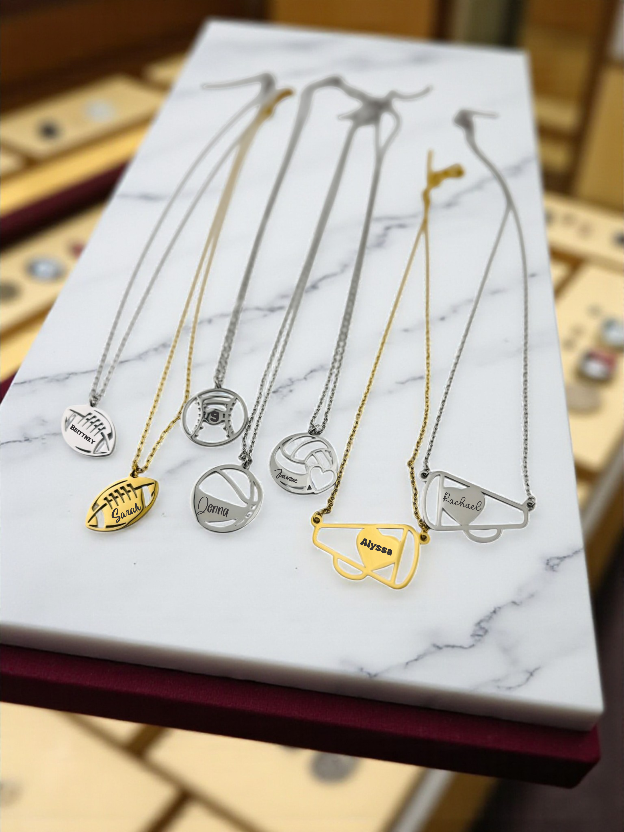 a collection of necklaces with various designs, including sports-themed pendants, arranged on a marble surface.
