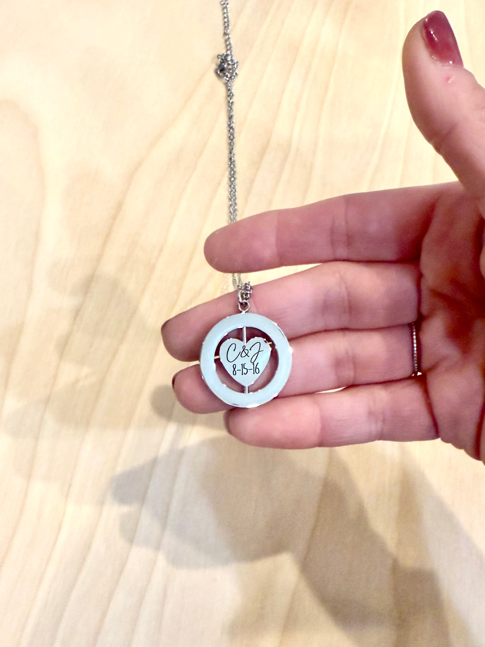Hand holding a necklace with a heart-shaped pendant on a light wooden surface