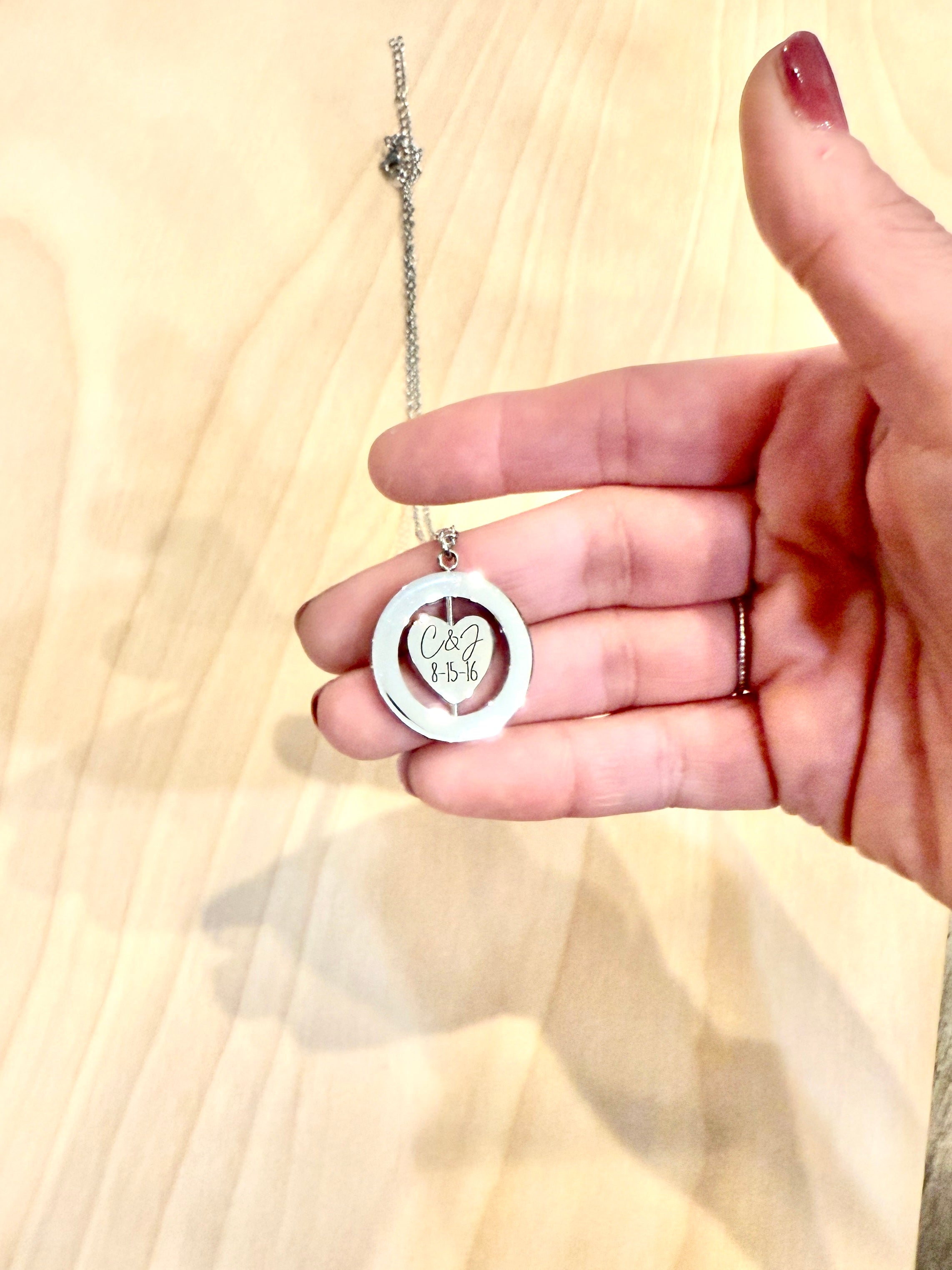 Hand holding a necklace with a heart-shaped pendant on a wooden surface