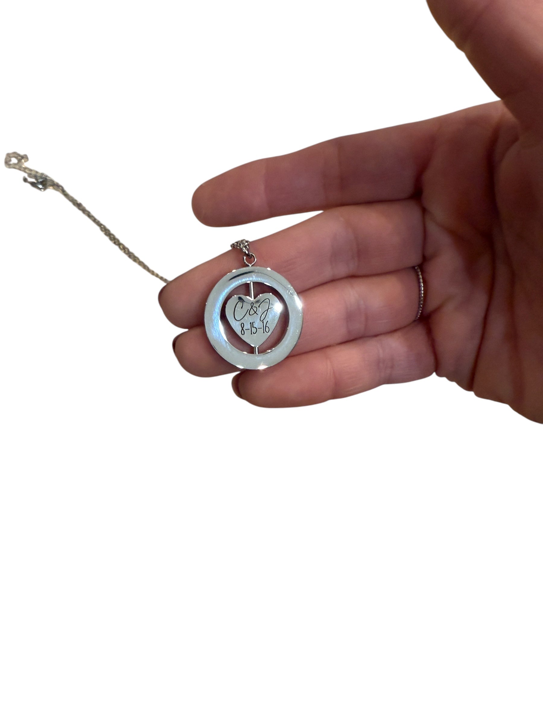 Hand holding a silver necklace with a heart-shaped pendant on a white background