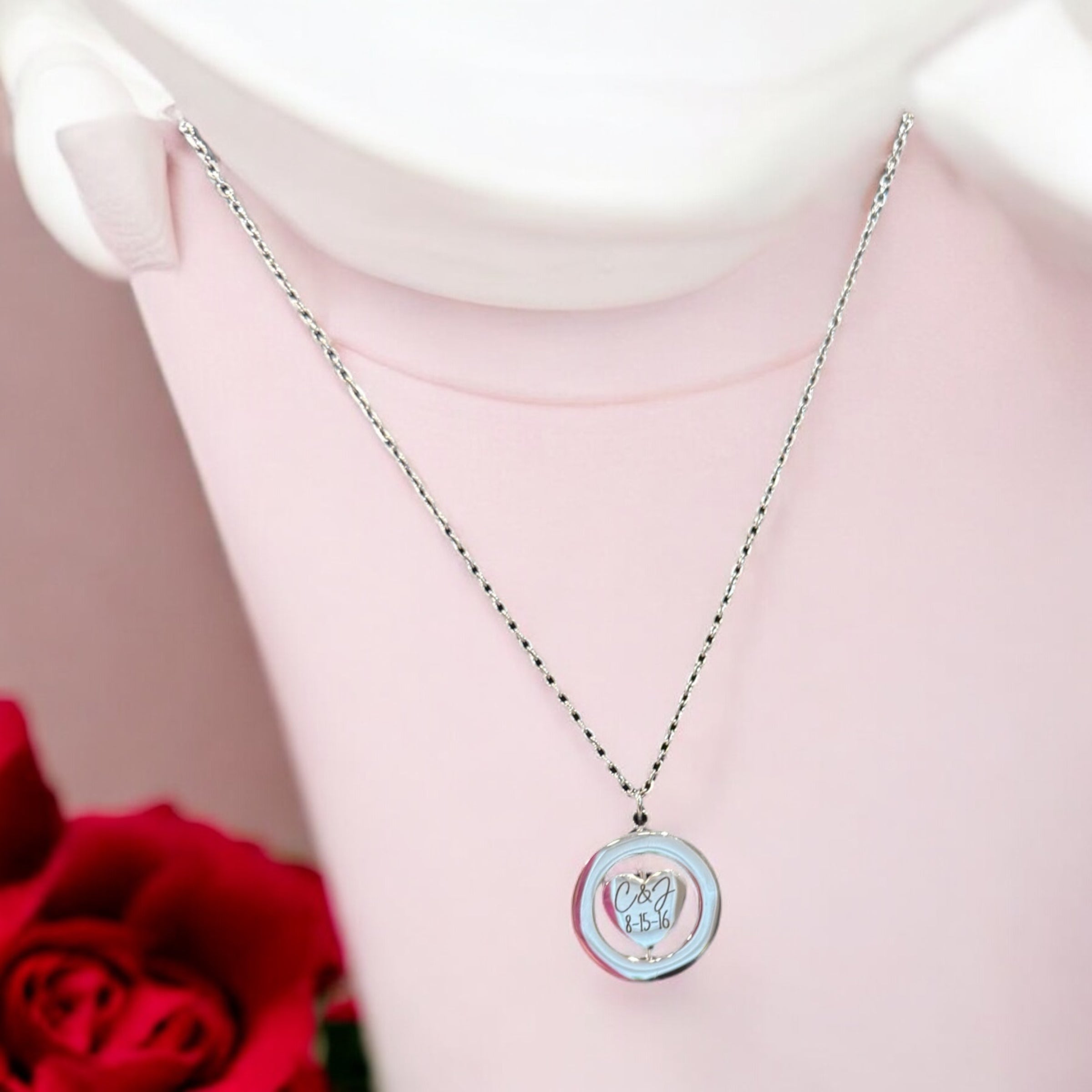 Necklace with a circular pendant on a pink surface with a red rose in the background