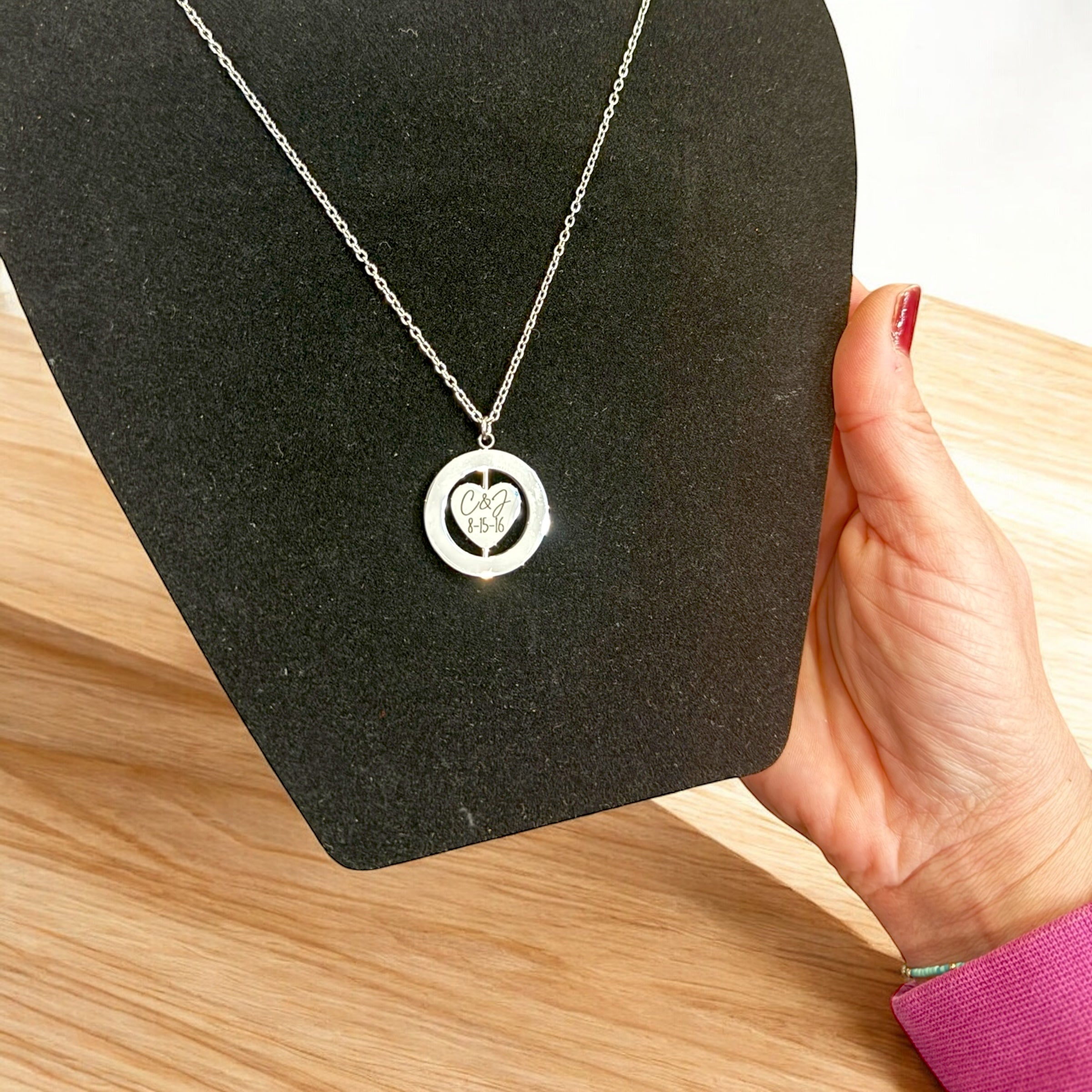Silver necklace with a heart pendant held by a hand on a black stand.